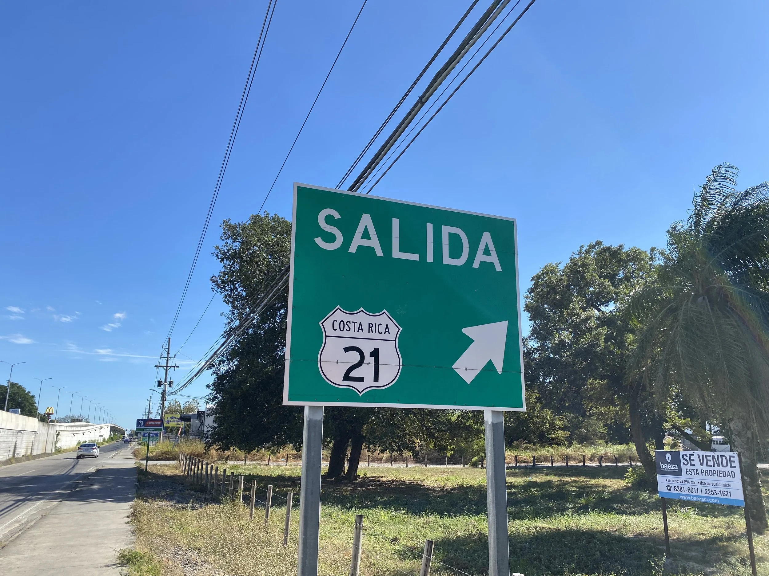 Road sign for Route 21 in Liberia, Costa Rica, beside a quiet roadside on a sunny day.