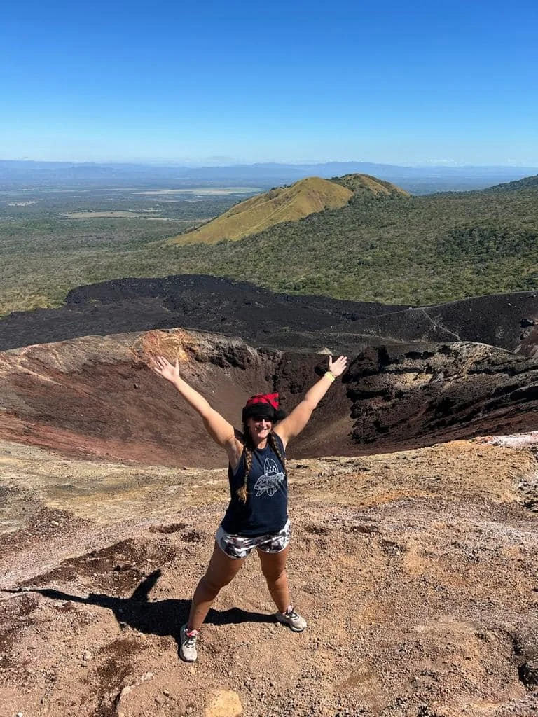 Woman standing on top of a volcano in Nicaragua with a wide landscape view of untouched nature and volcanic terrain