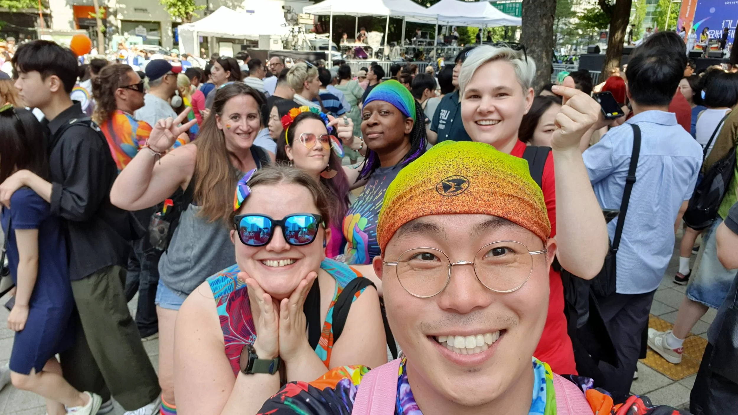 A group of friends smiling together at Seoul Pride surrounded by crowds and rainbow clothing.