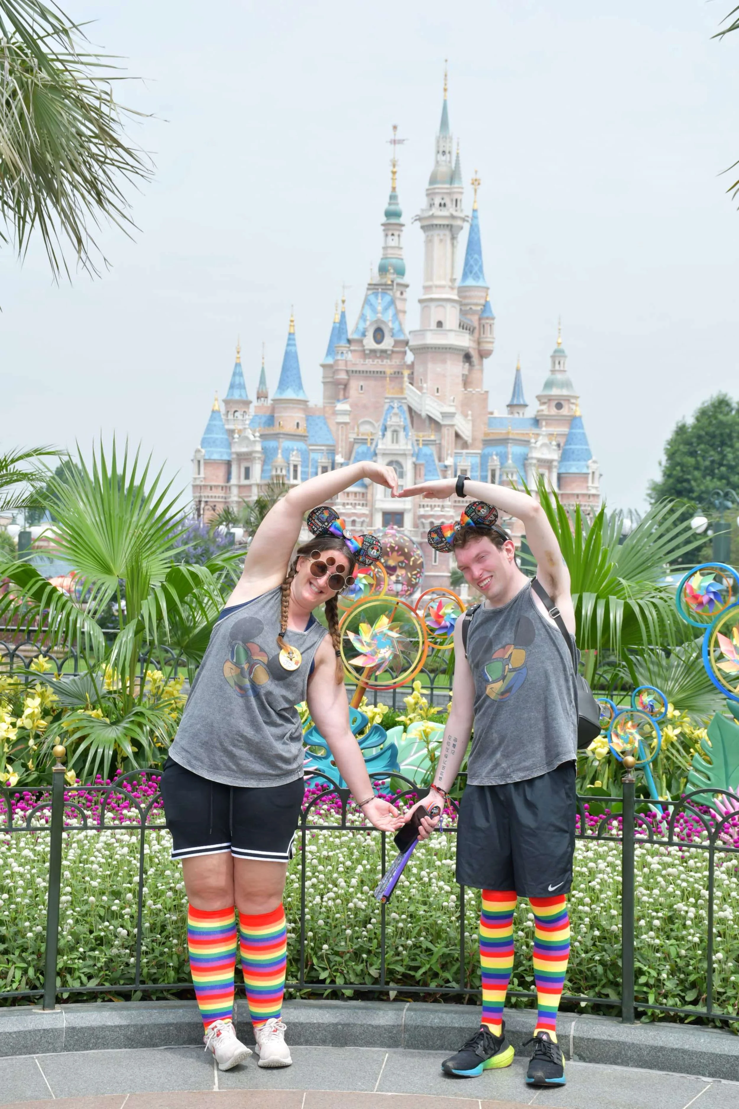 Two people wearing rainbow socks and Disney ears posing in front of Shanghai Disneyland castle during Pride.