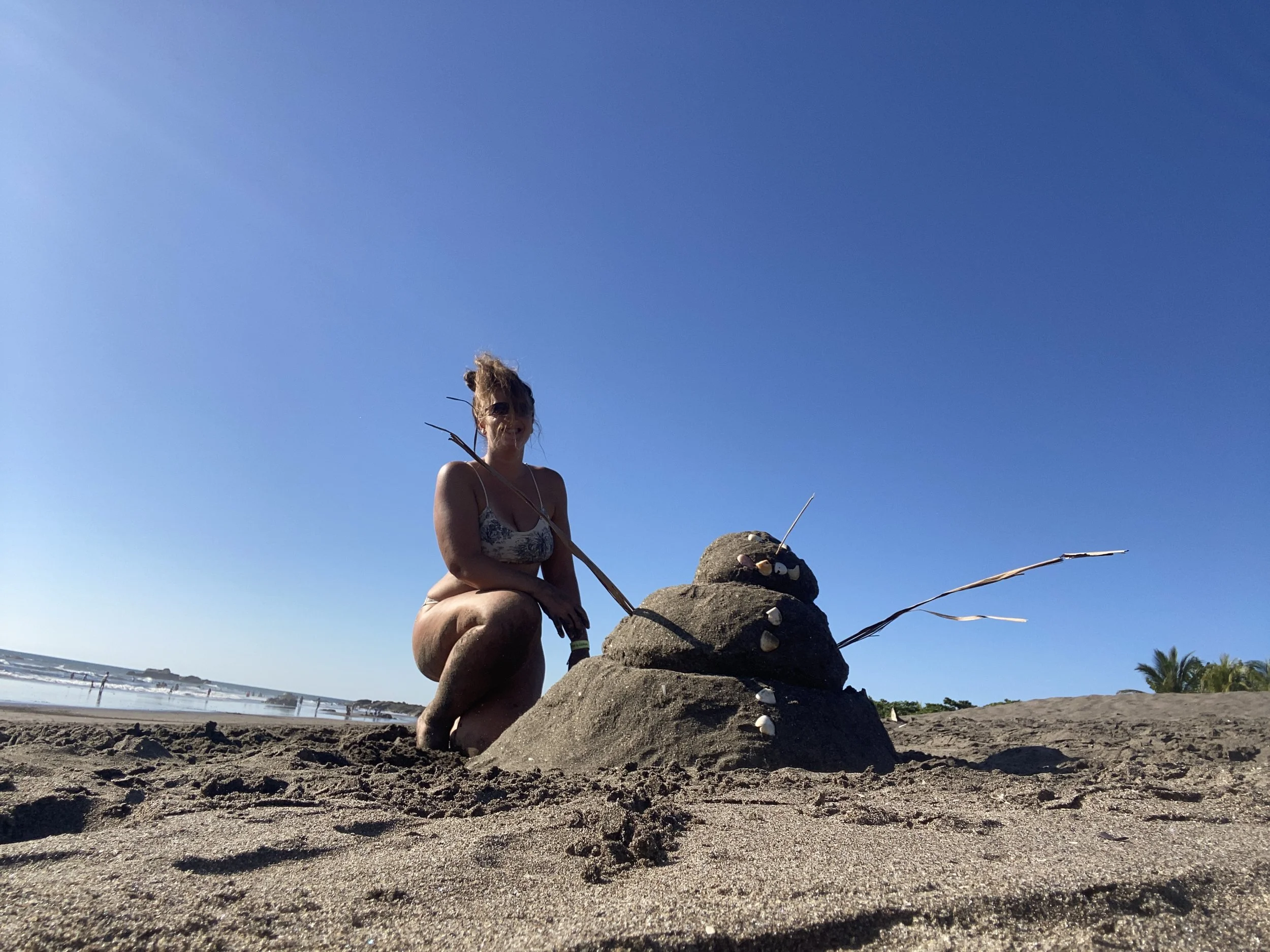 Solo female traveler posing with a handmade sandman decorated with shells on a beach in Nicaragua