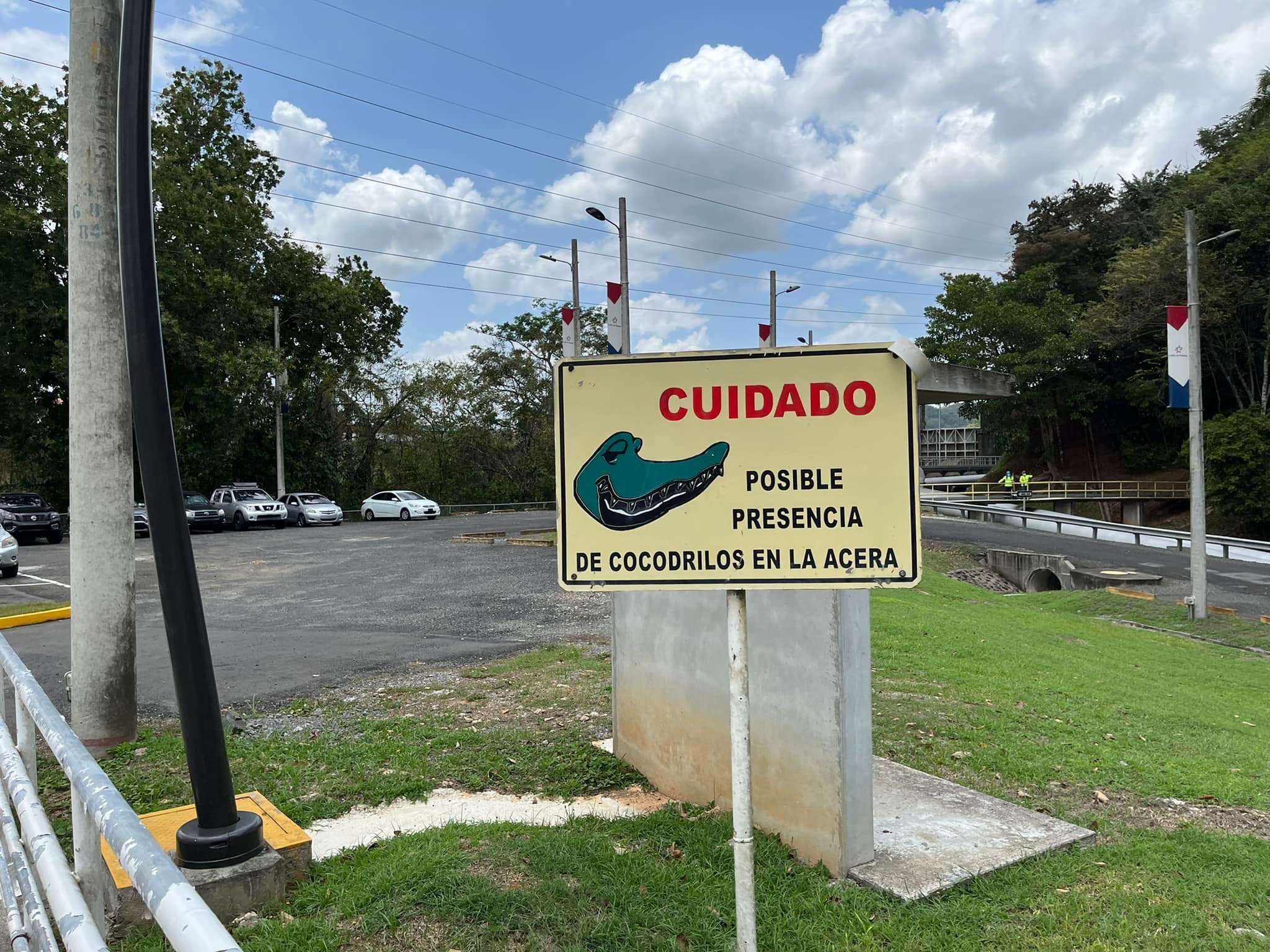 Spanish warning sign reading “Cuidado: posible presencia de cocodrilos en la acera” beside a road in Panama.