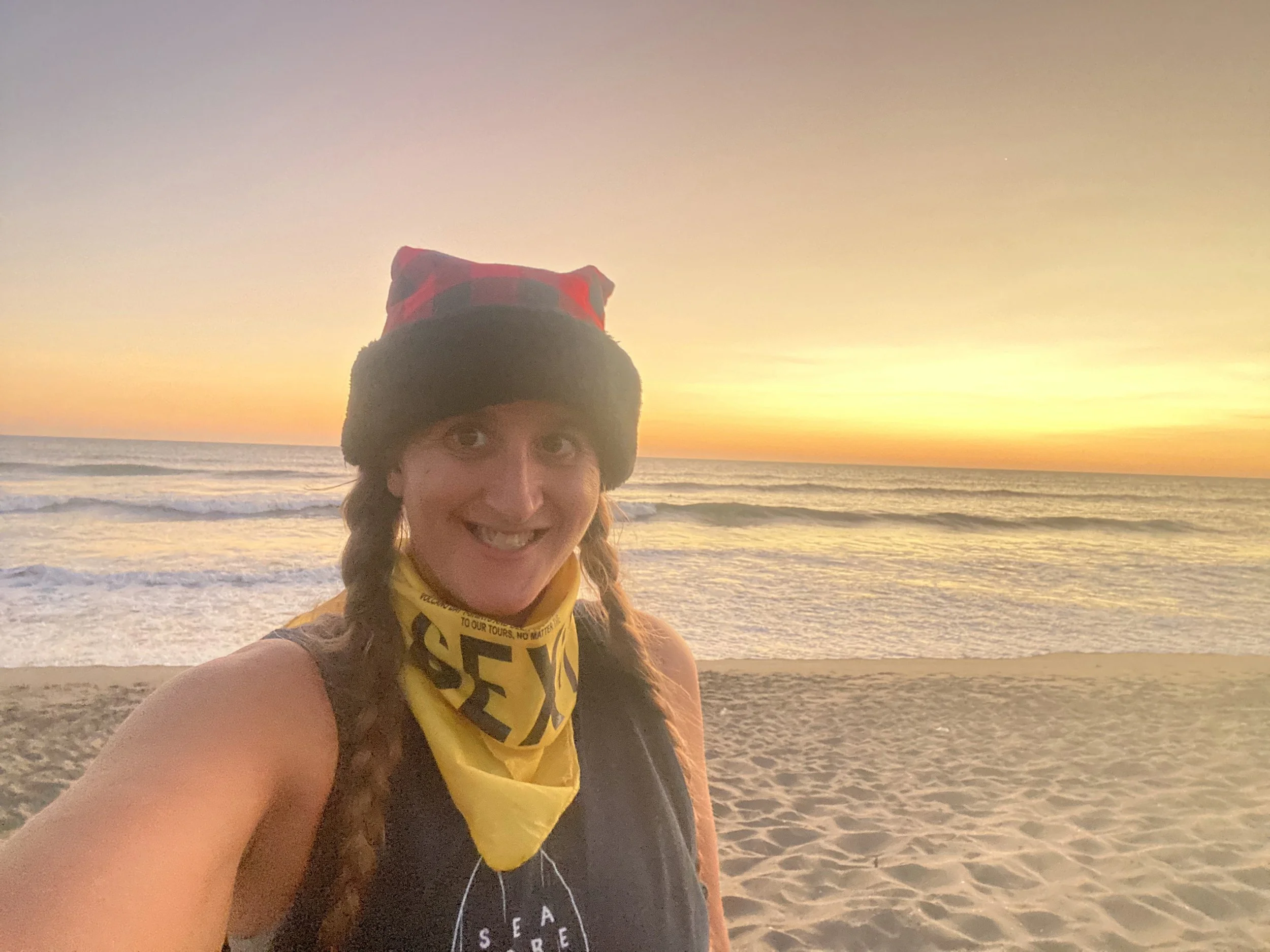 Woman smiling on Las Peñitas beach at sunset, with orange sky, ocean waves, and sandy shoreline in the background.