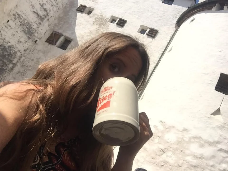 Female traveller drinking from a large beer stein while exploring a sunny European destination.