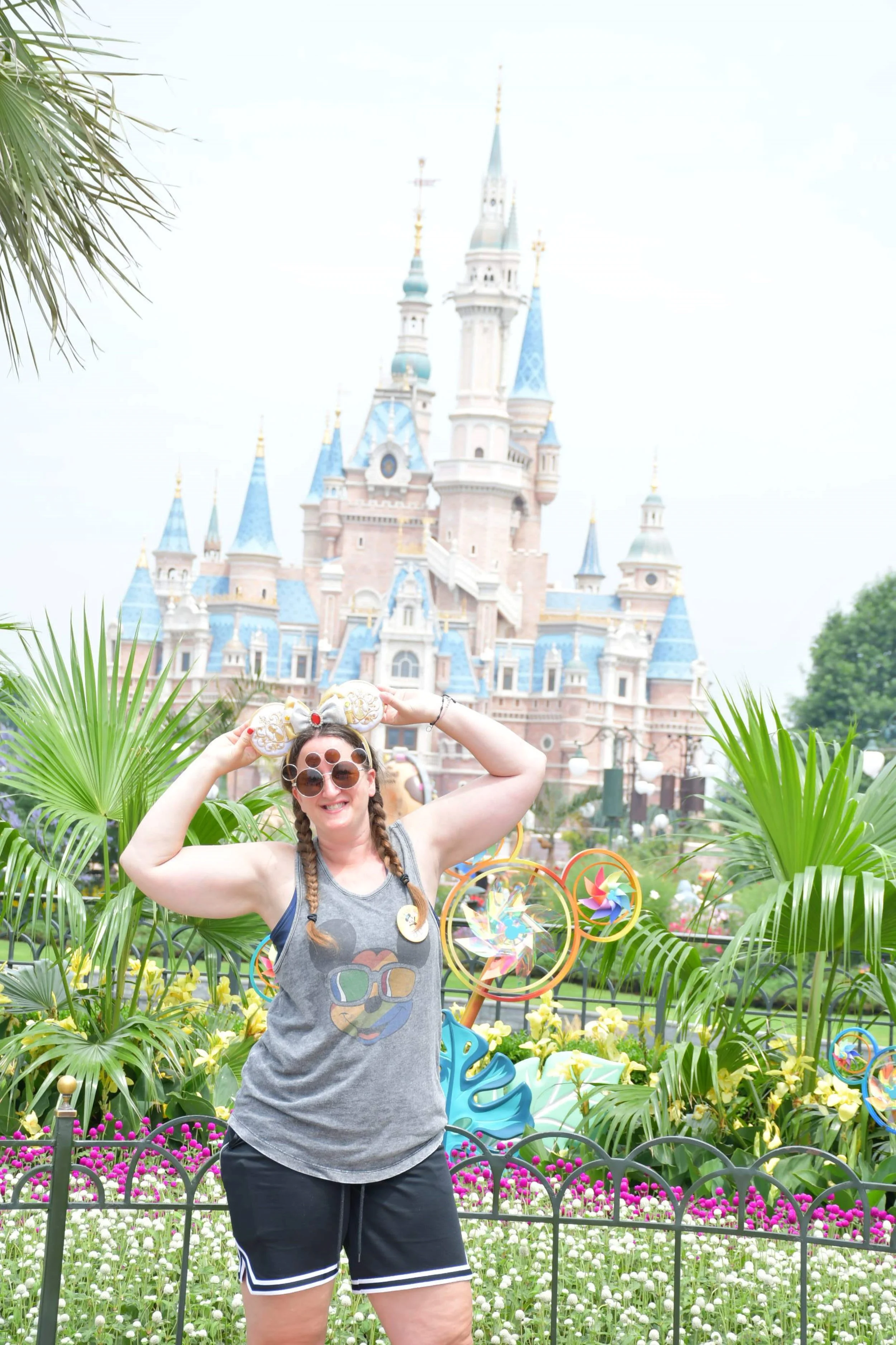 A traveler wearing Mickey-themed accessories posing in front of Shanghai Disneyland Castle.