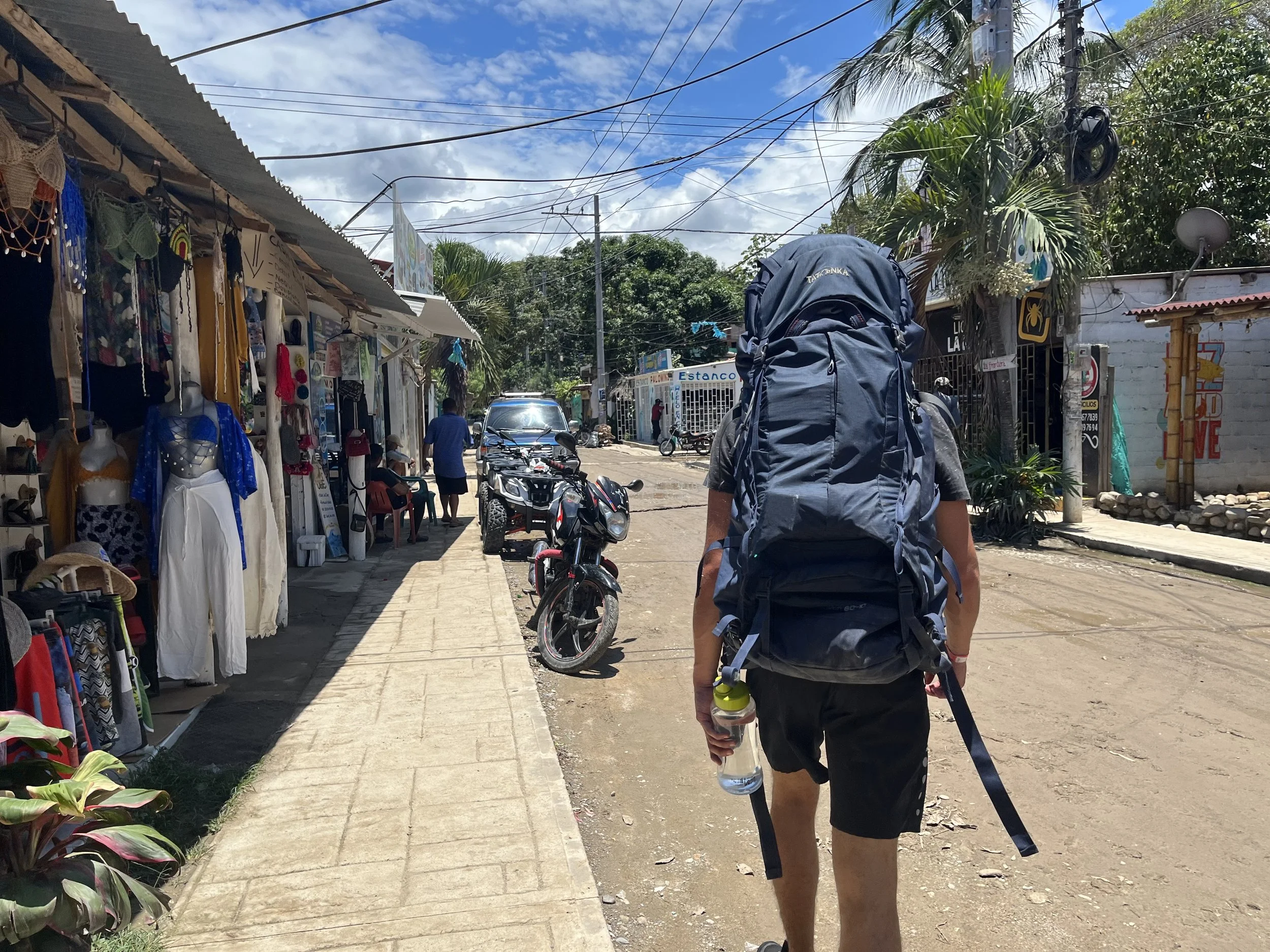 Solo backpacker walking toward the main road to catch a local bus before discovering that a wallet was missing from a backpack.