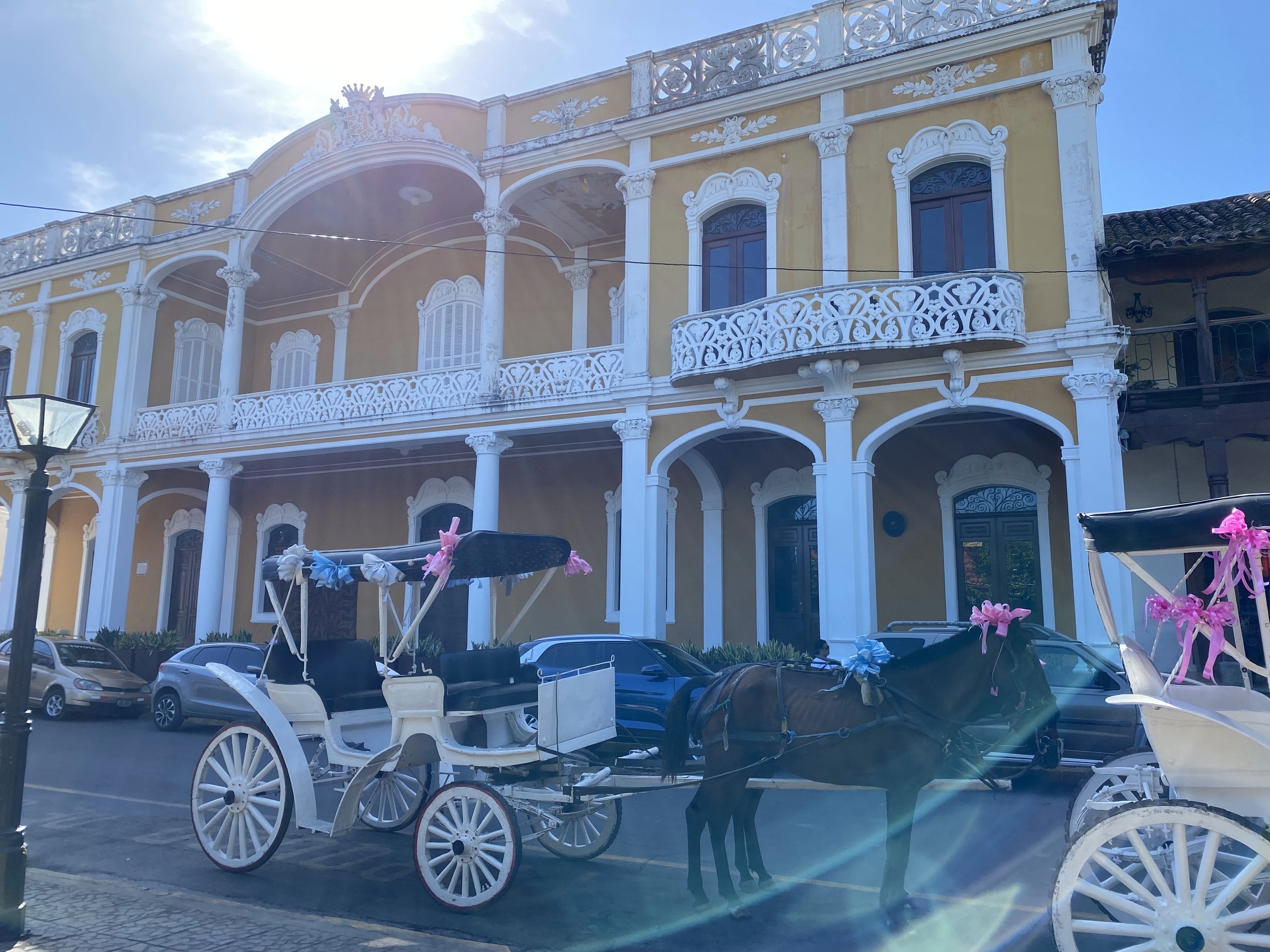 Horse-drawn carriage parked in front of a yellow colonial building in Granada, Nicaragua, with sunlight shining over the historic architecture.