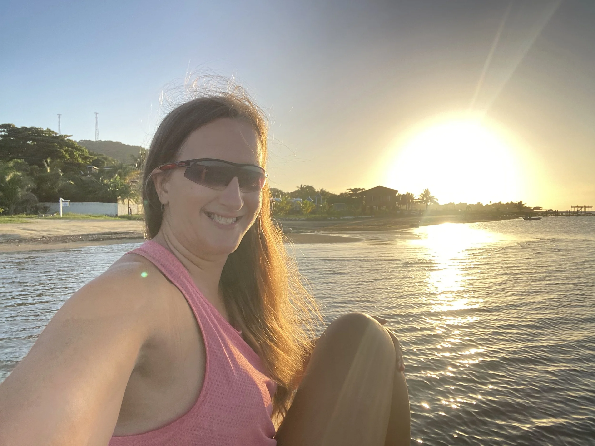Jamie watching sunset on the beach in Roatán, Honduras with golden light over the Caribbean Sea