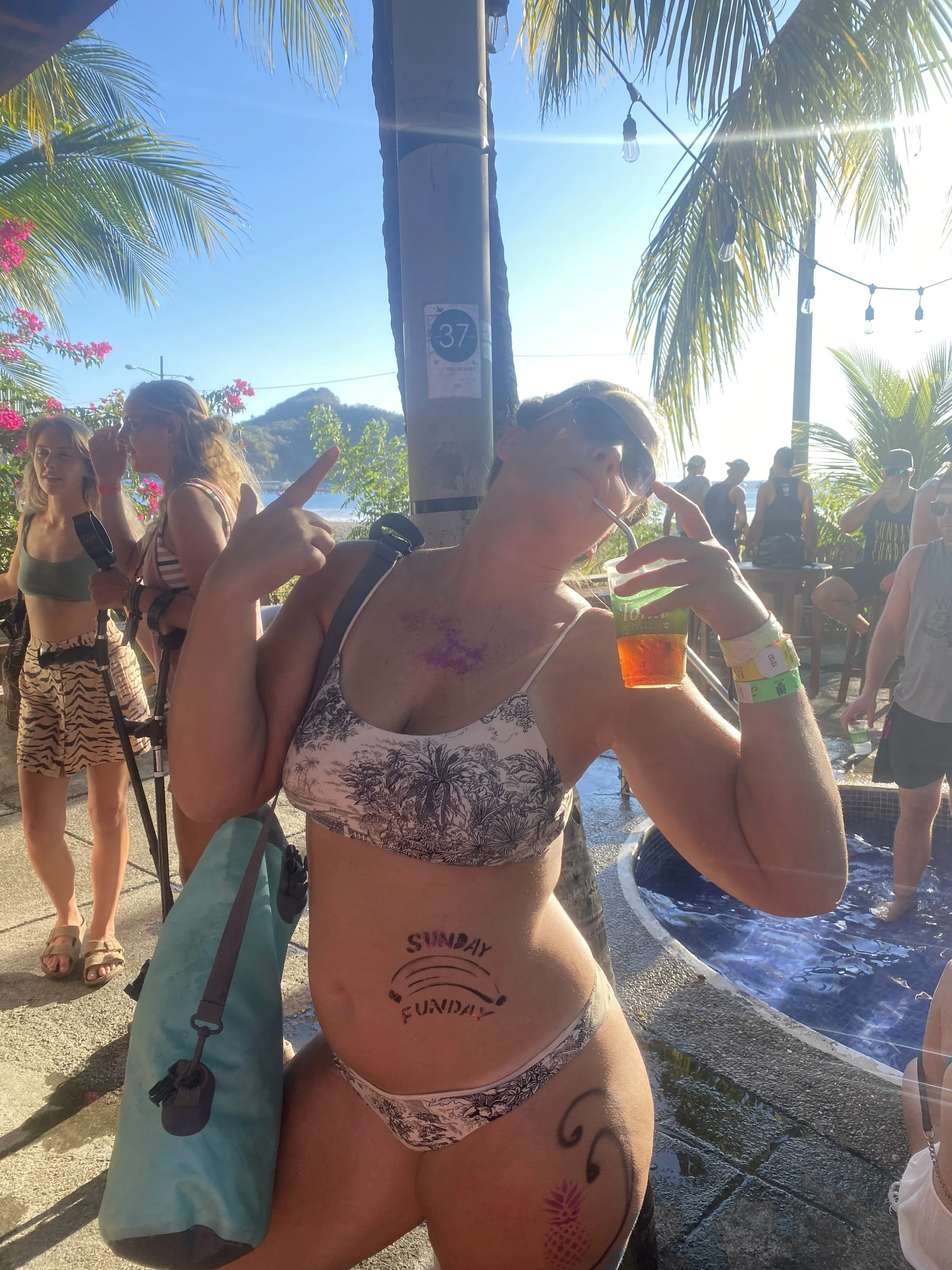 Traveler covered in glitter and temporary body paint enjoying Sunday Funday in San Juan del Sur, Nicaragua, with a drink in hand.