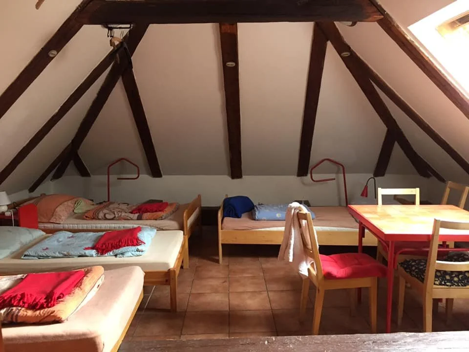 Shared hostel room in Český Krumlov, Czech Republic, with several single beds, wooden ceiling beams, a table and chairs.