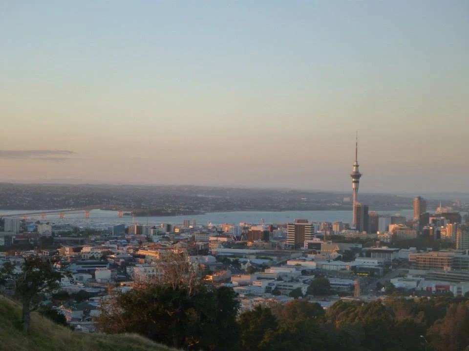 Auckland city skyline at sunset with the Sky Tower and harbour in the distance.