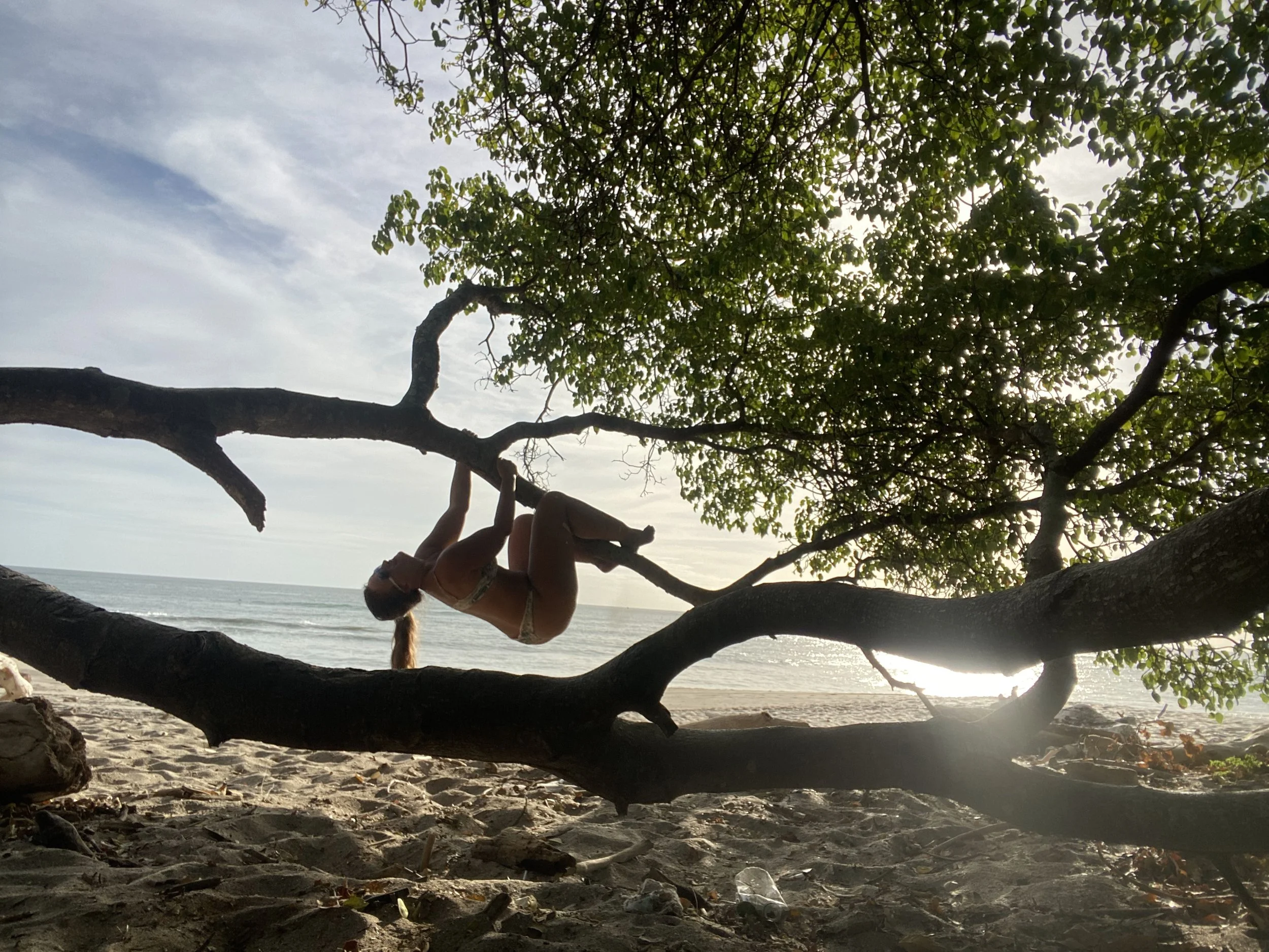 Solo female traveler climbing a tree on a beach in Nicaragua to relax in the shade near the ocean