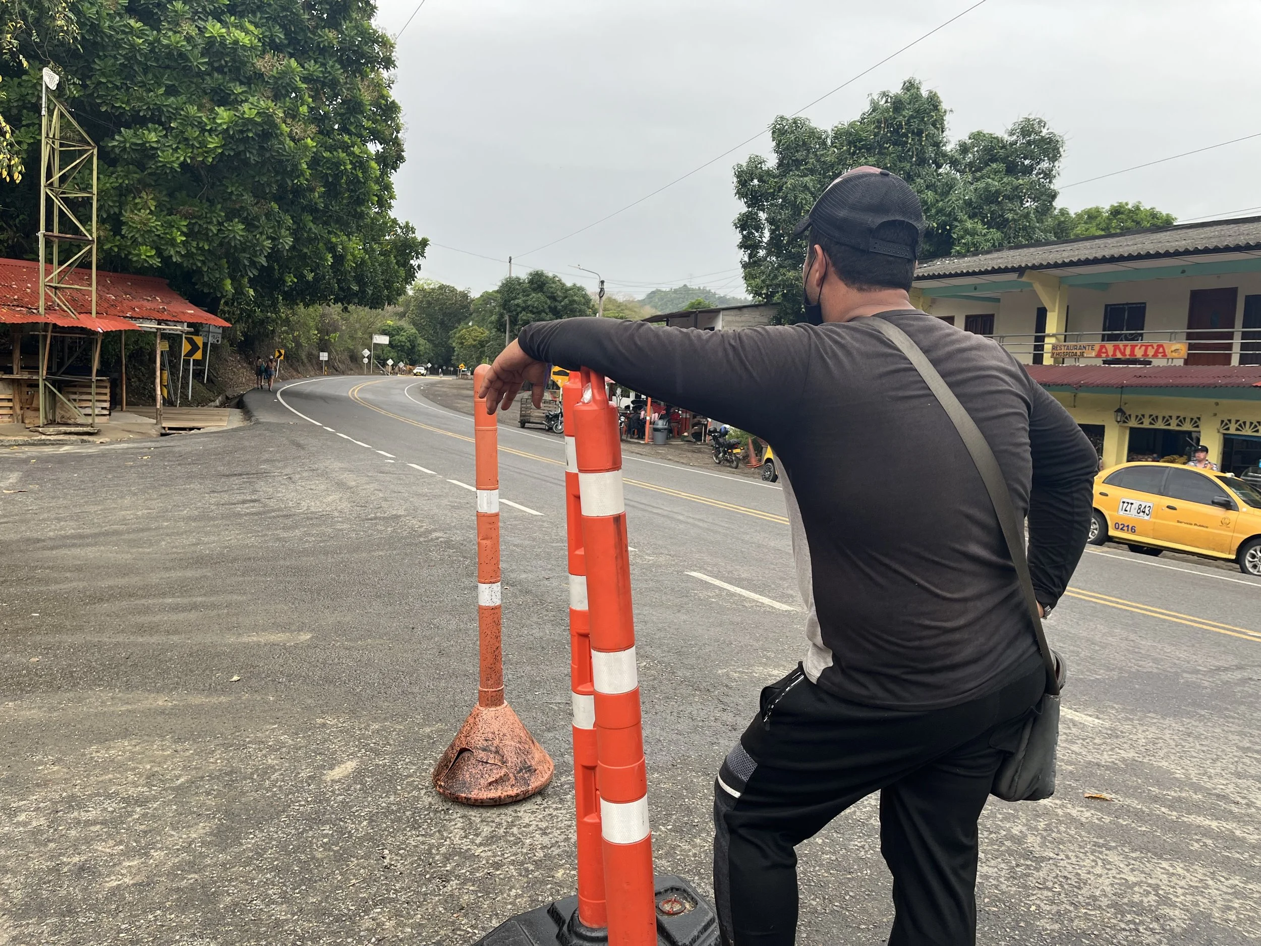 Bus attendant waiting beside a highway in Colombia after accidentally unloading a traveler's backpack at the wrong stop, highlighting the importance of storing valuables in separate places while traveling.
