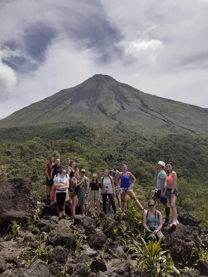 Tour group standing on volcanic rocks with Arenal Volcano rising in the background near La Fortuna, Costa Rica.