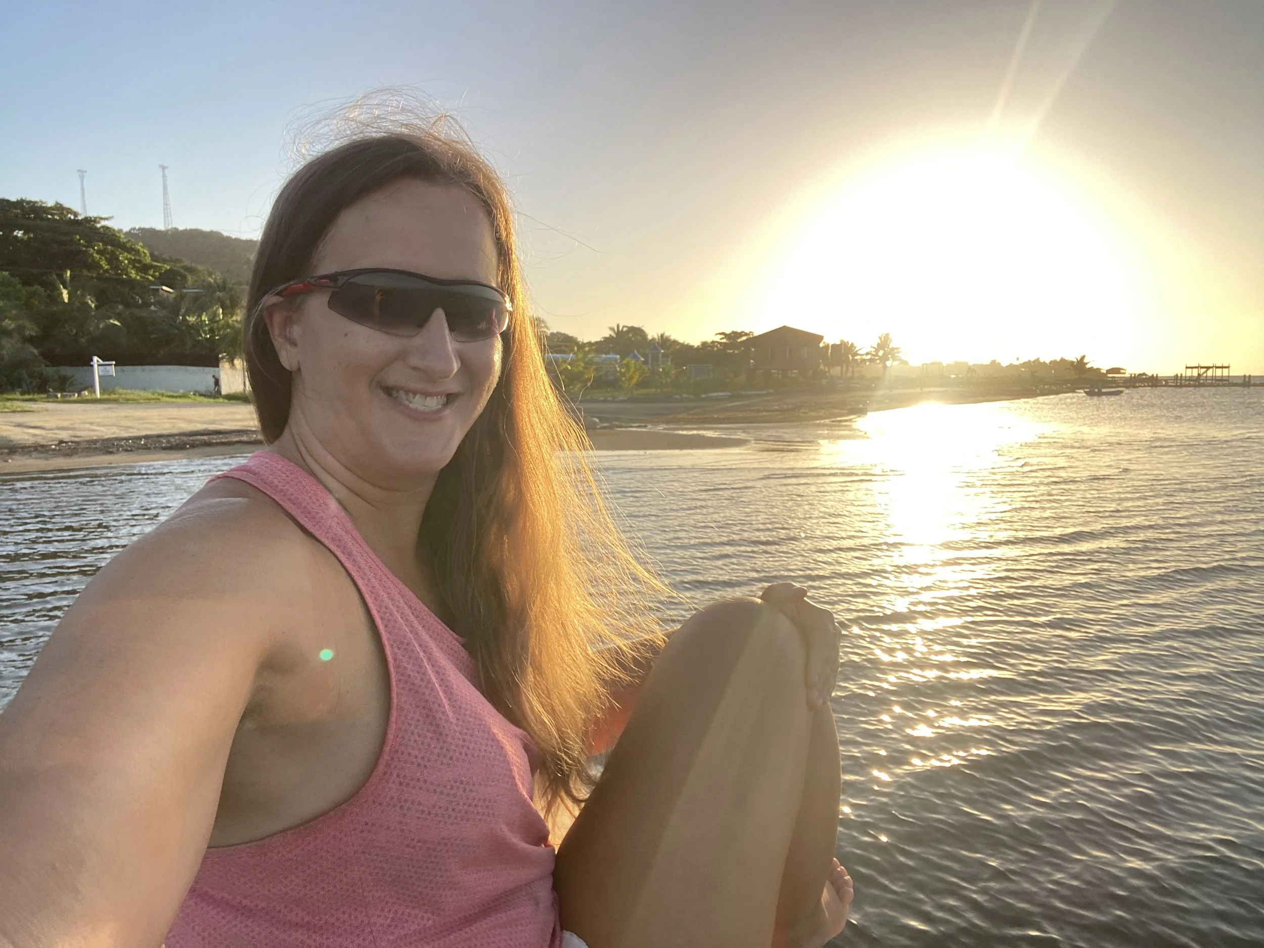 Woman sitting by the water in Roatán, Honduras at sunset with golden light reflecting on the ocean