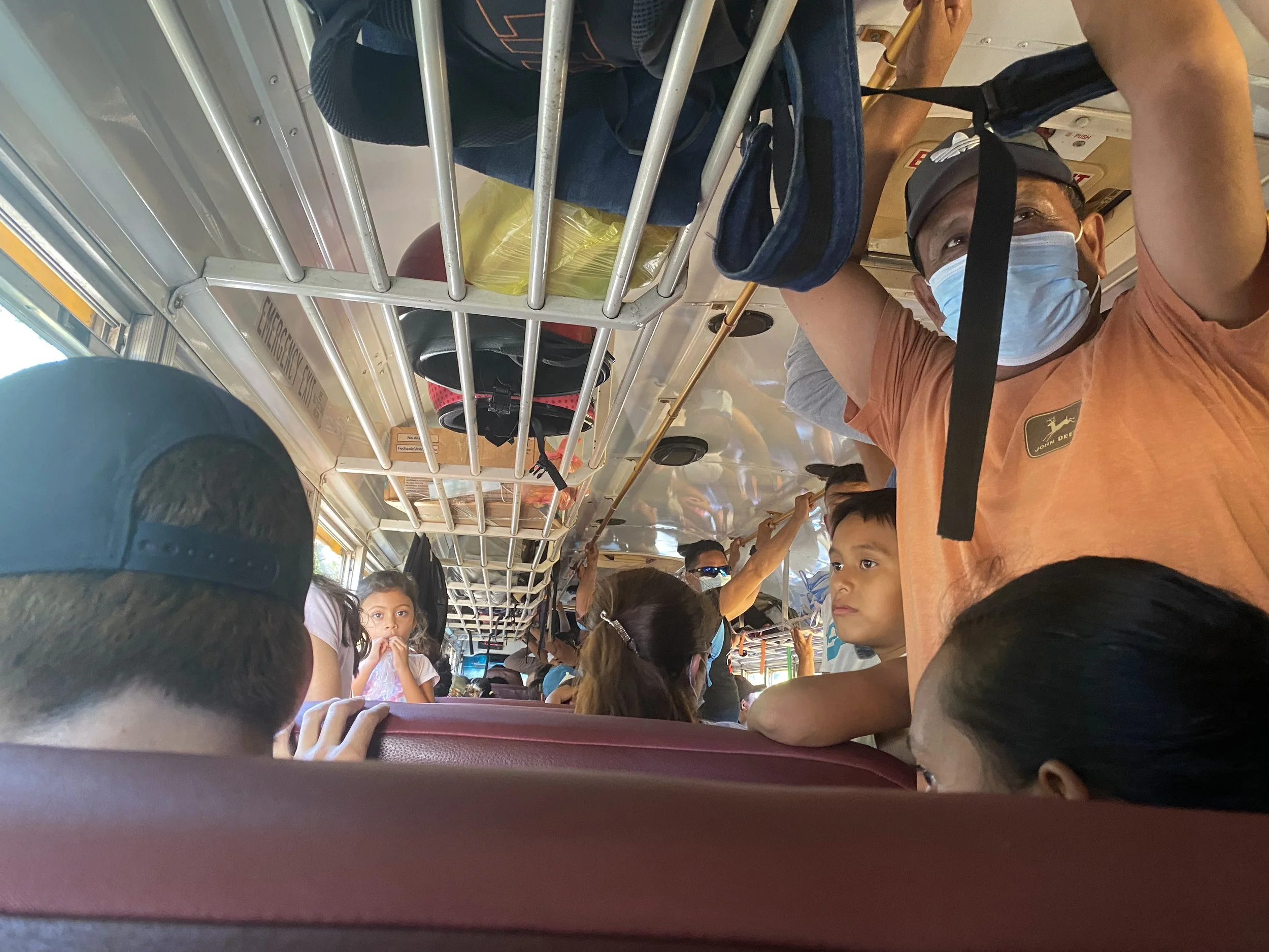 Local crowded bus in Nicaragua with passengers seated and standing, bags stored overhead during the ride from León to Las Peñitas