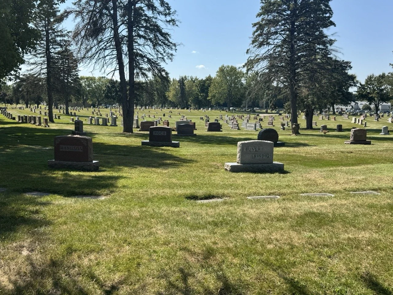 Headstones across open cemetery lawn with trees