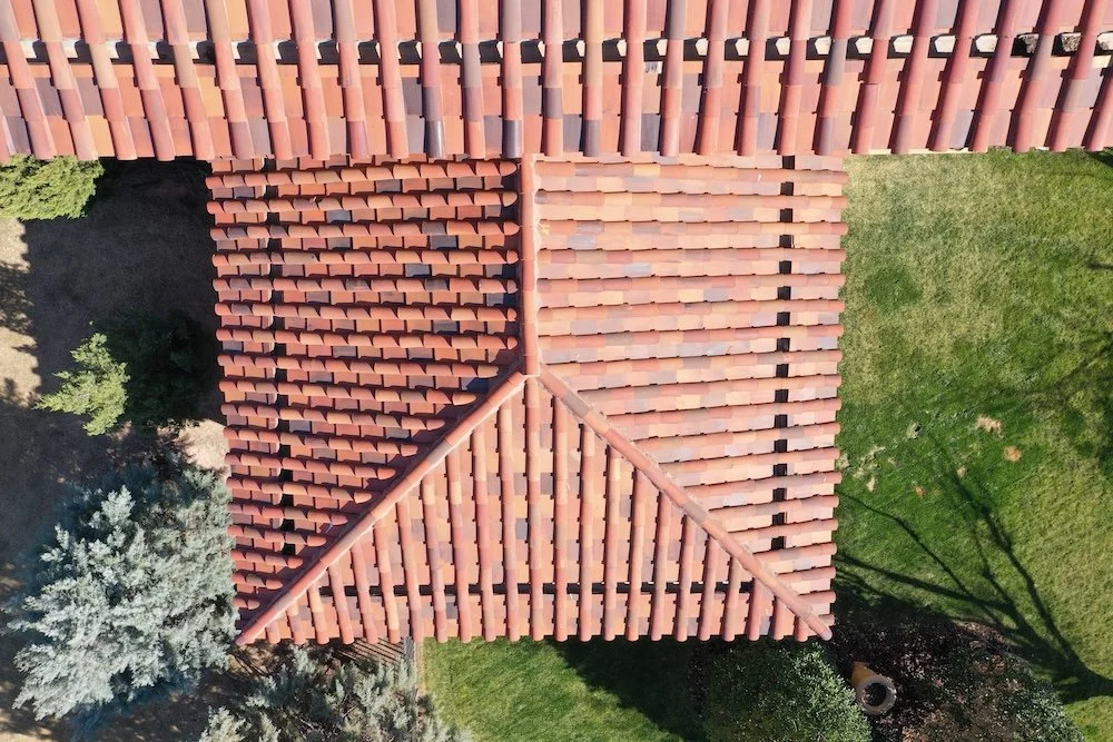 An aerial view of a building with a red tiled roof and surrounding green grass and trees.