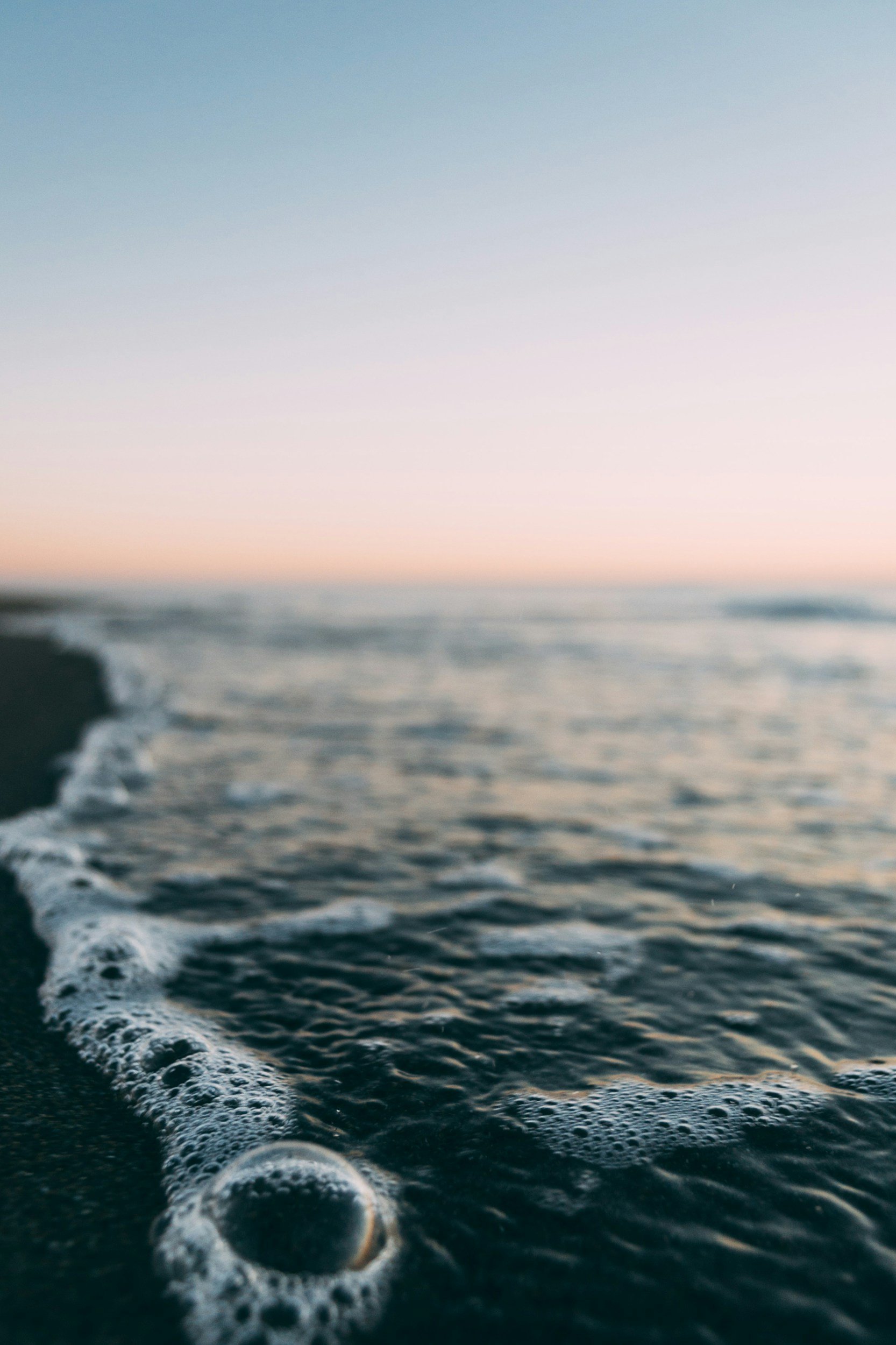 Ocean waves crashing on the shore at sunset, with a soft pastel sky in the background.