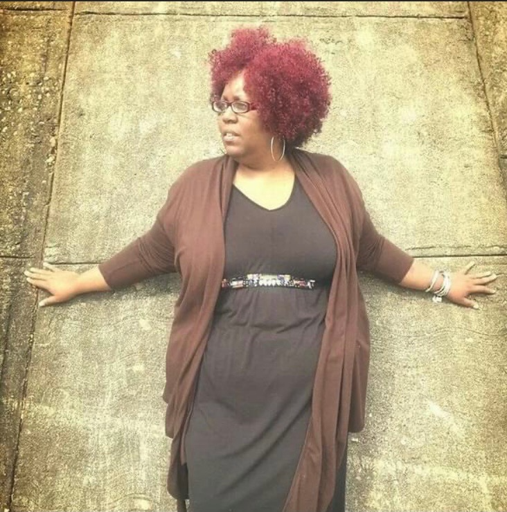 Woman with curly red hair and glasses lying on a concrete sidewalk with arms stretched out to the sides.
