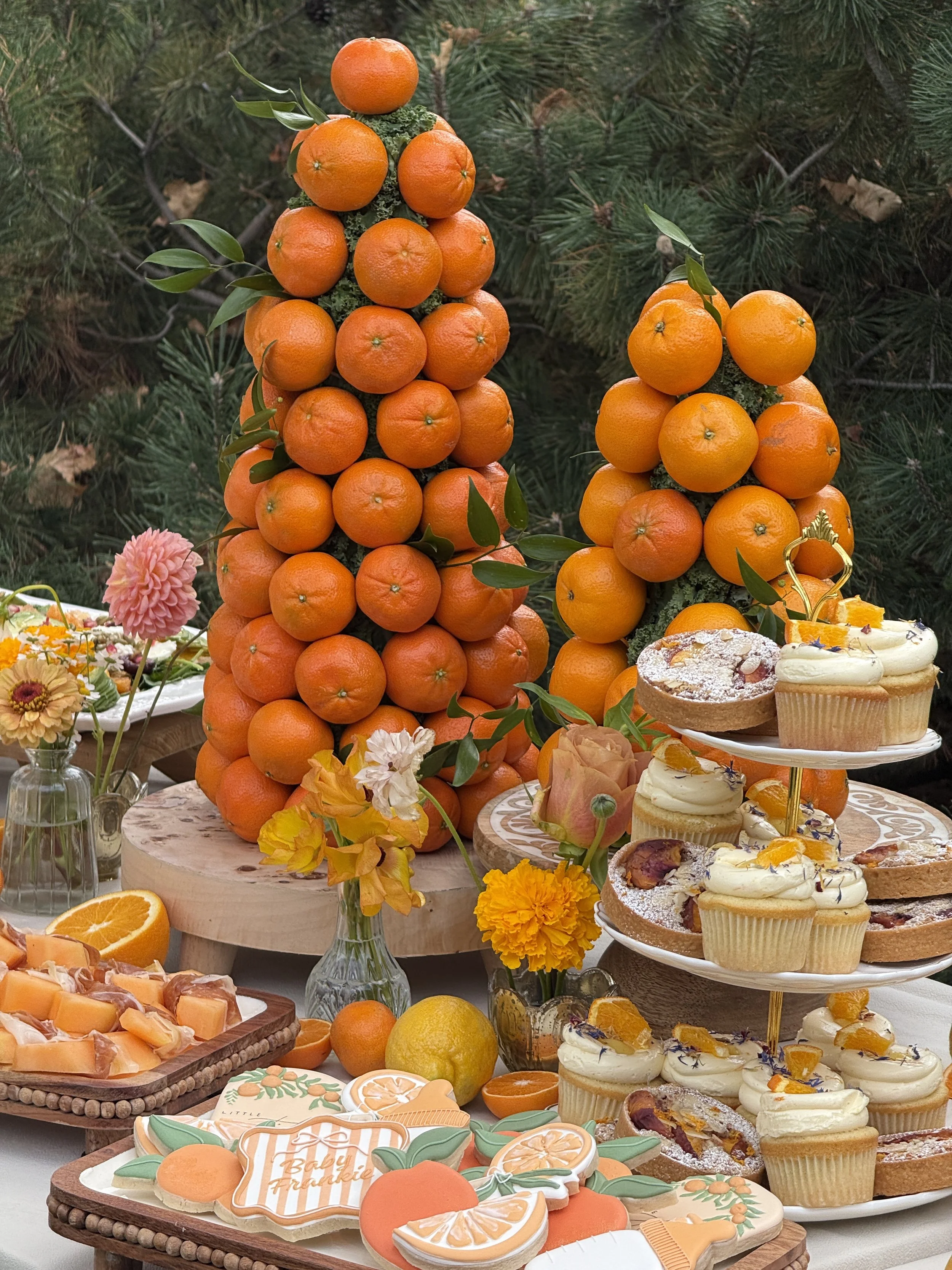 Decorative orange clementines and cupcakes on a table with flowers.