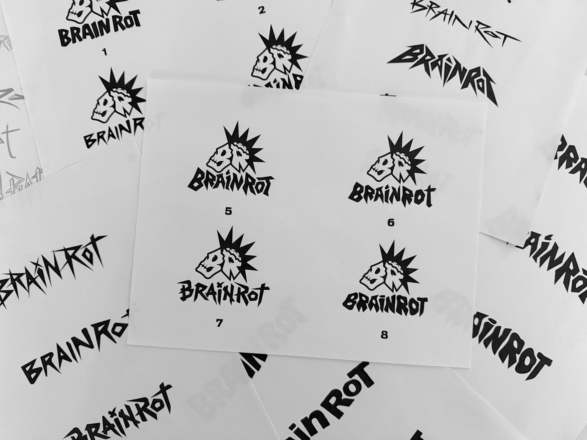 Multiple sheets of paper with a black and white logo featuring a skull with a mohawk and the text "BRAIN ROT" in stylized font.