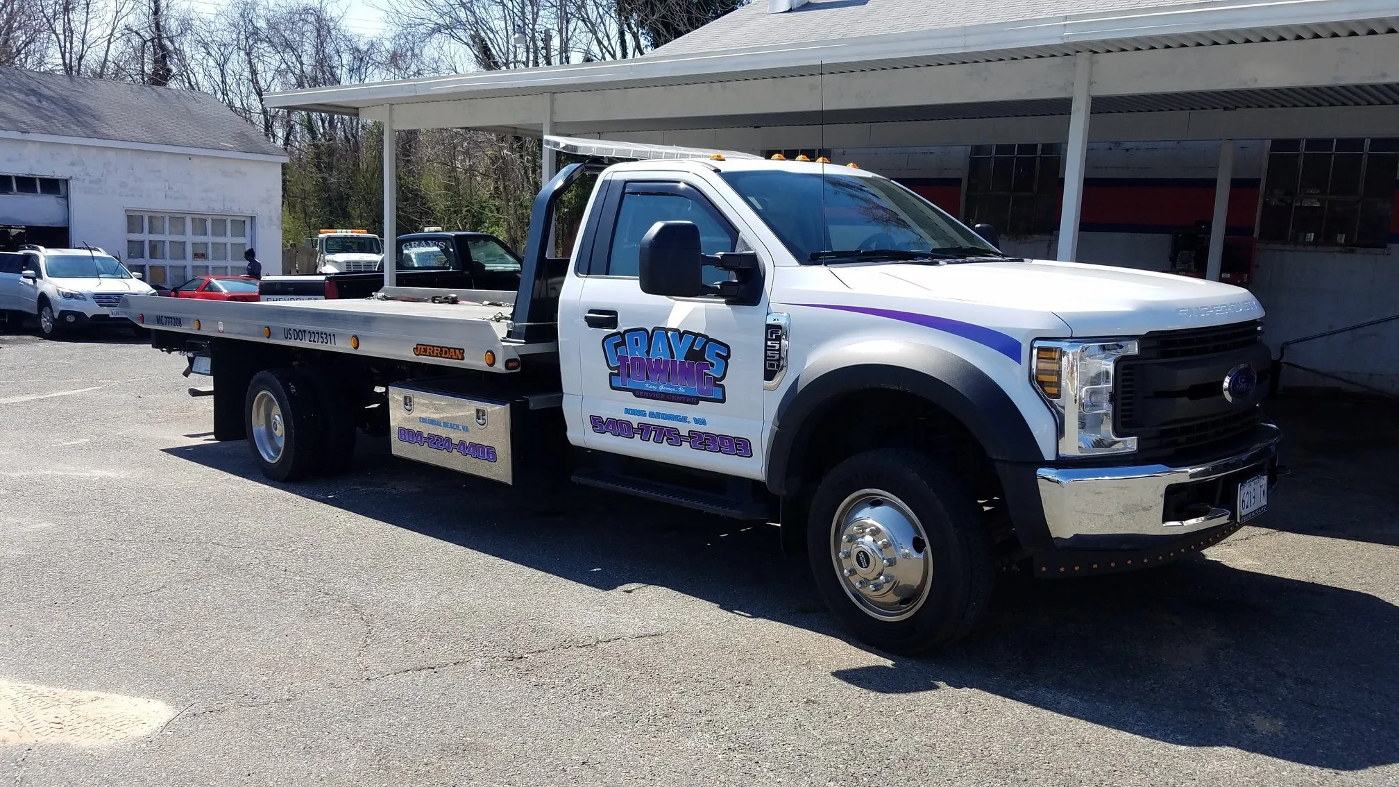 White tow truck branded with custom vinyl vehicle graphics and lettering with 'Gray's Towing' logo and contact information parked in a lot.