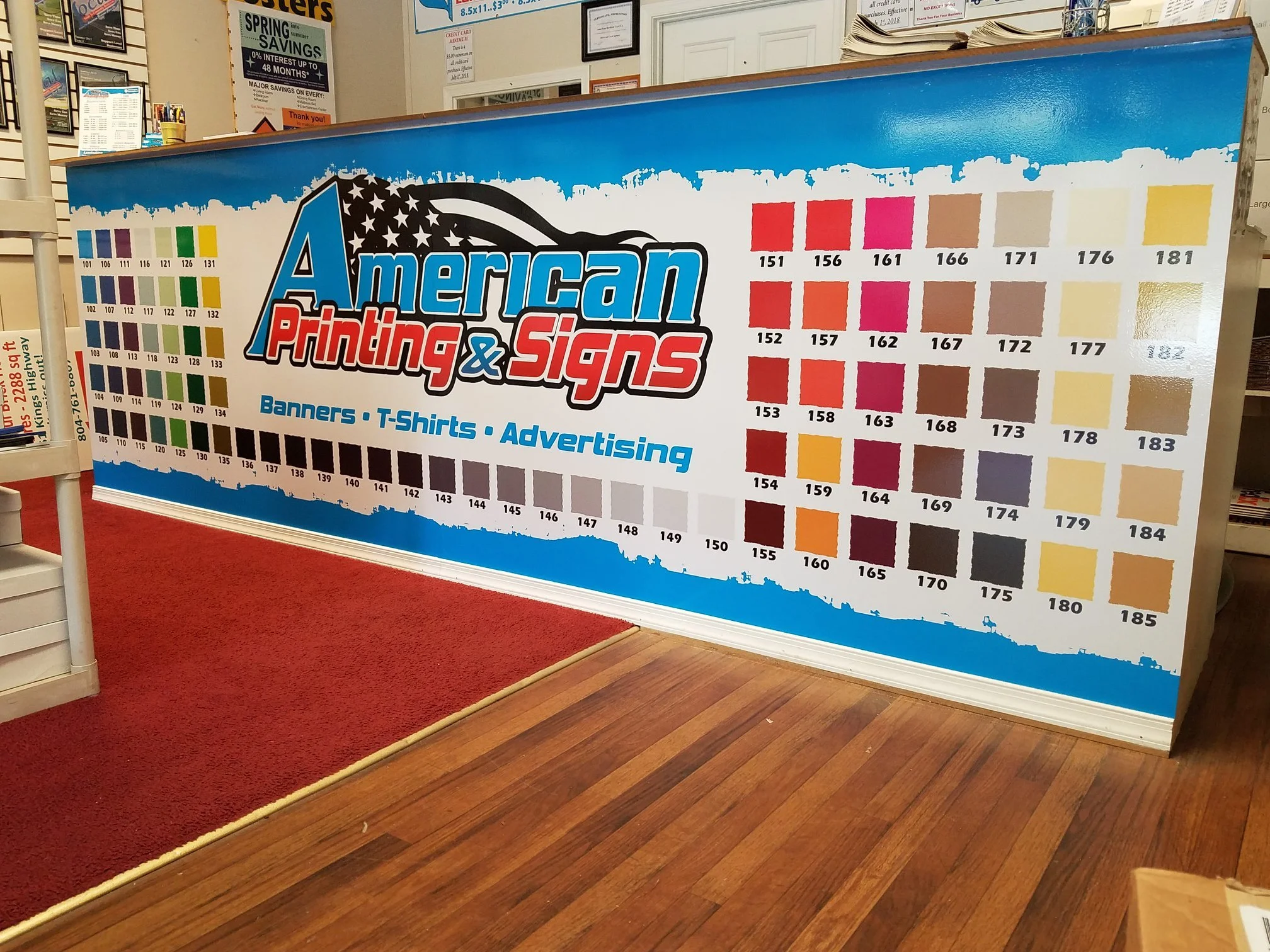 A large display board for American Printing & Signs showing color samples, ink, and print swatches with color codes, advertising banners, T-shirts, and advertising services.