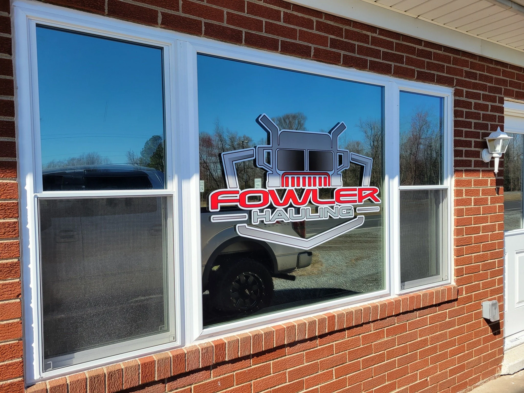 Front window of a brick building with a window decal graphic logo for Fowler Hauling.