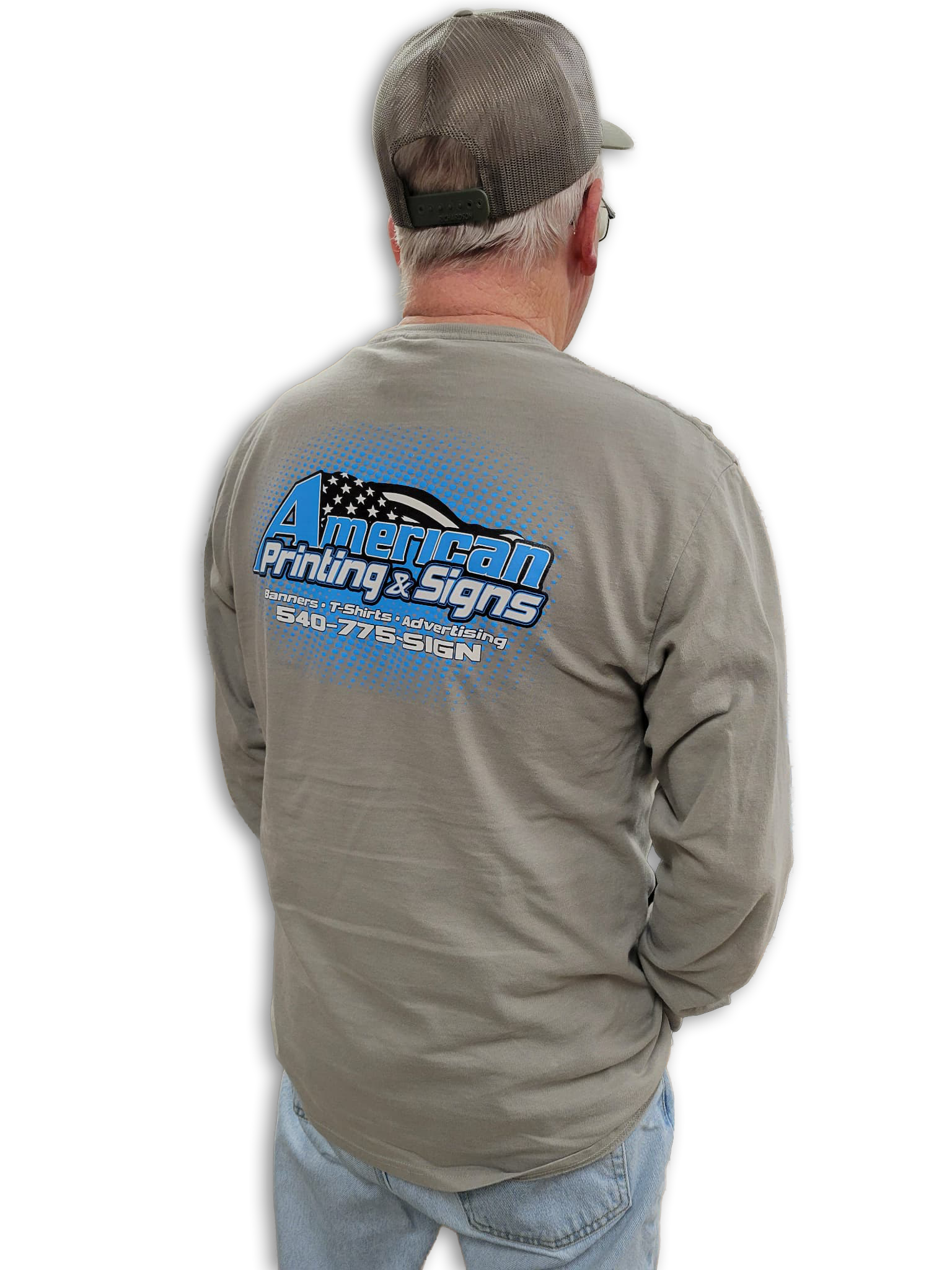 Back view of a man wearing a custom branded beige long-sleeve shirt with a company logo for American Printing & Signs on the back, along with a gray baseball cap and light blue jeans, against a black background.