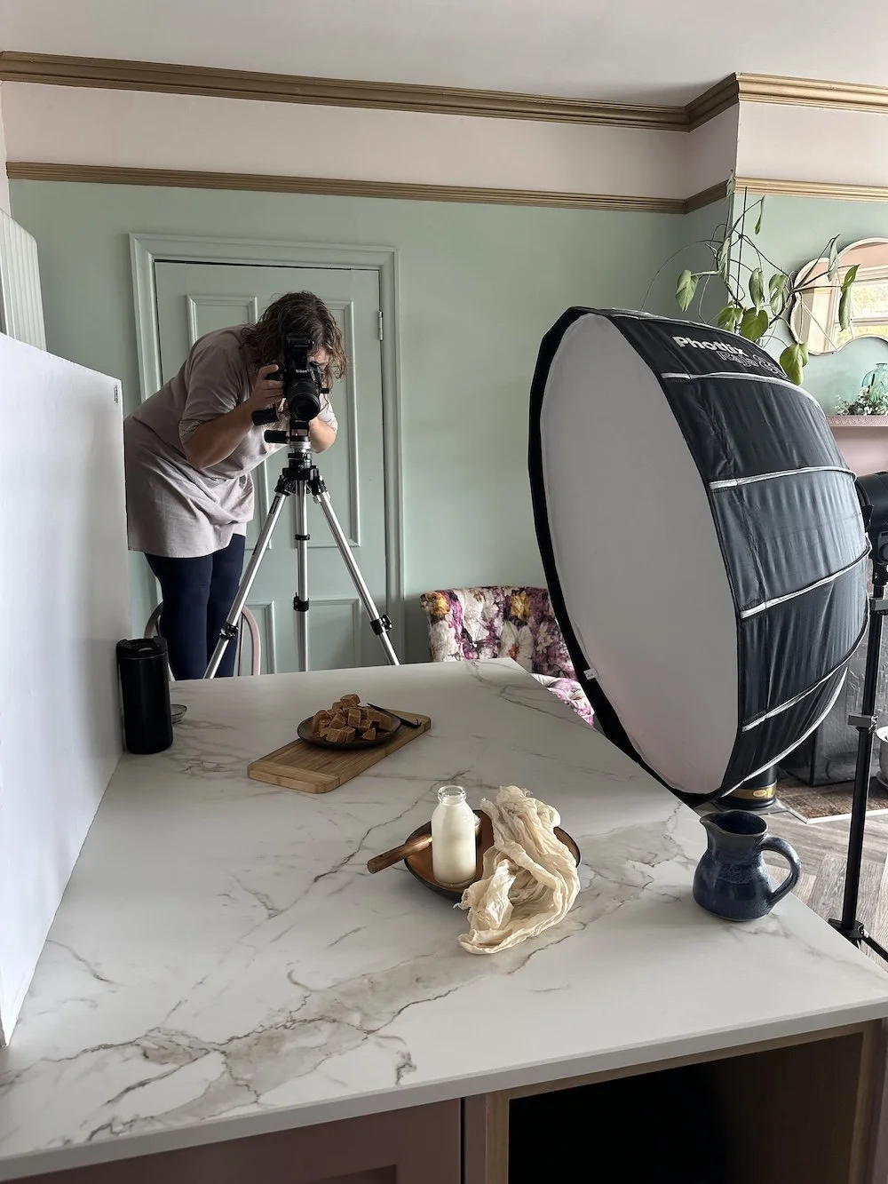 Photographer setting up a professional food and product shoot in a kitchen with softbox lighting and props