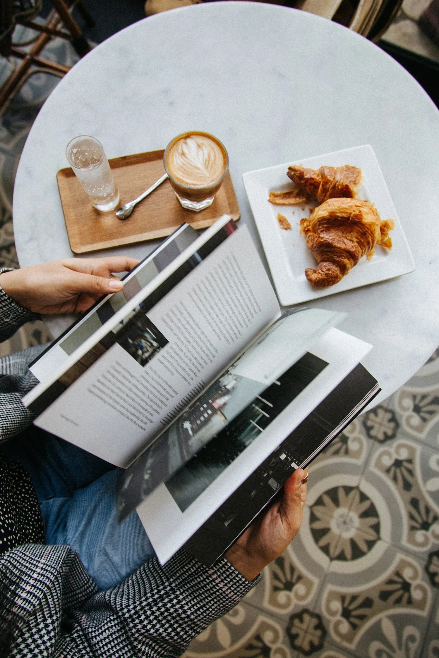 Café flatlay overhead view with a latte, croissant, notebook and magazine on a marble table