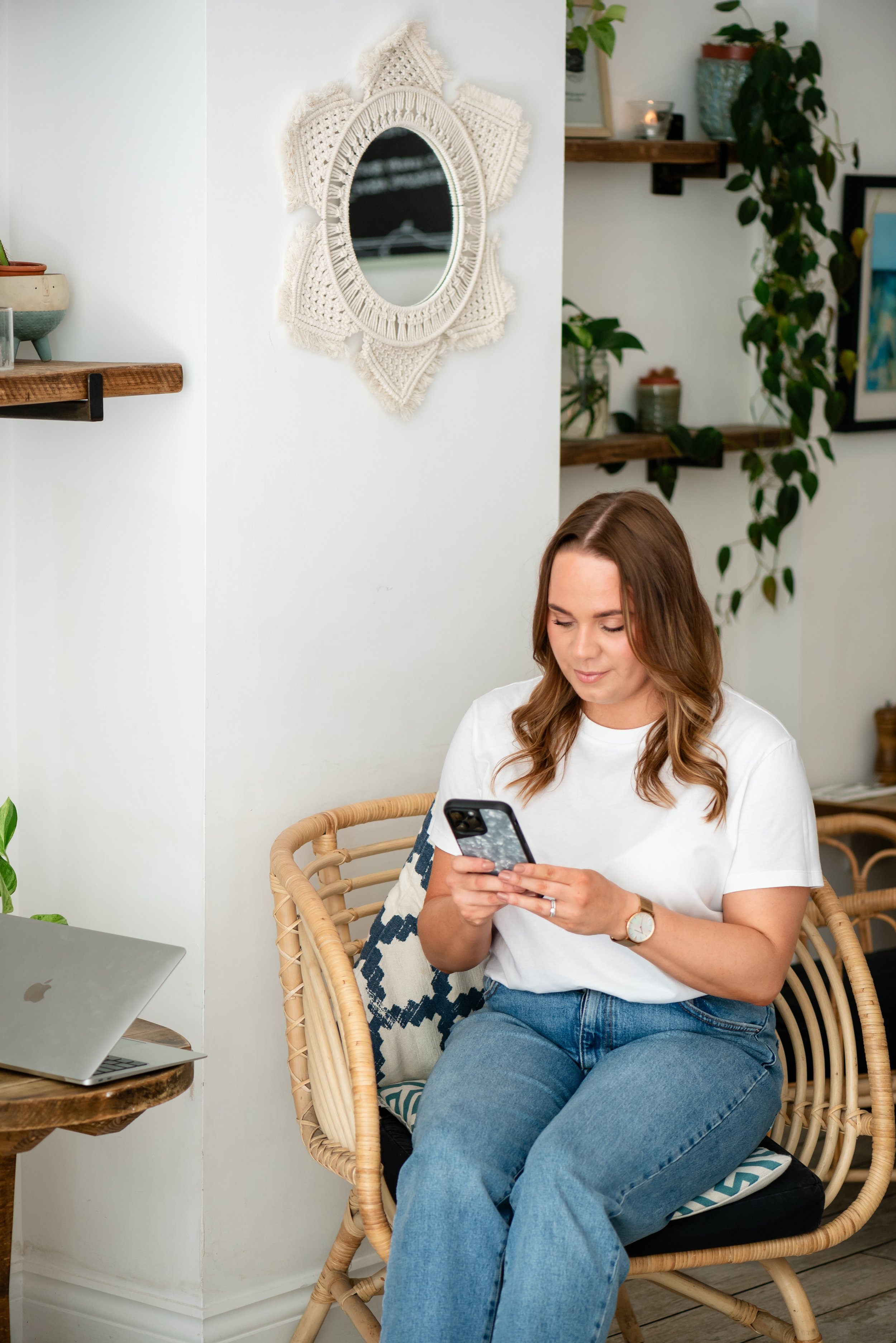 Grace from Silver Lining Social checking social media on her phone in a styled home workspace