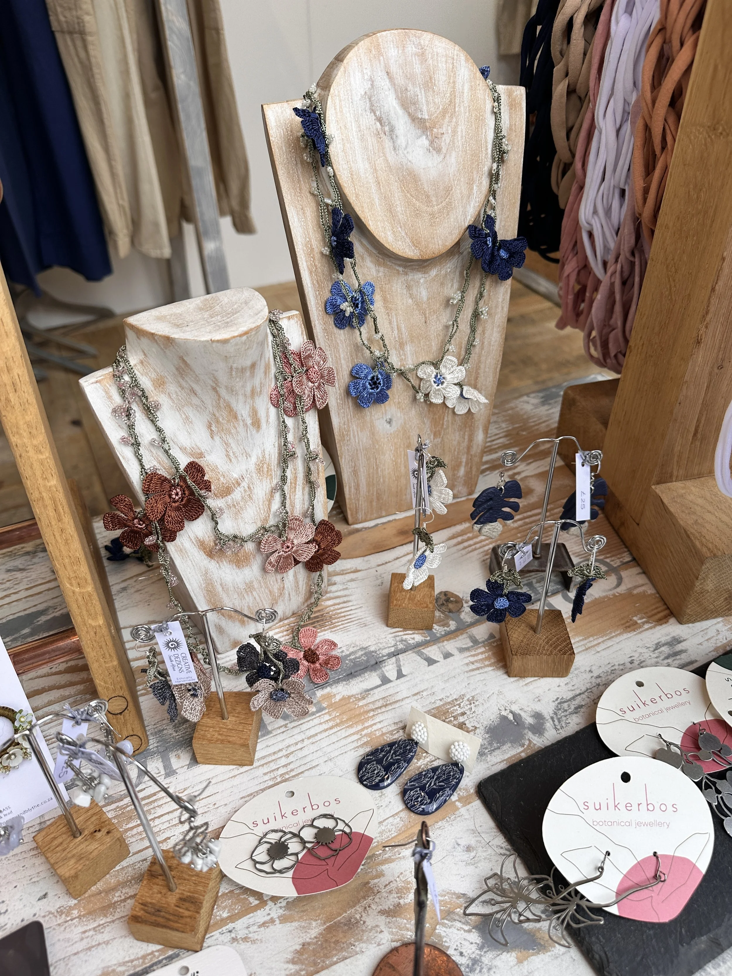 Independent jewellery brand display with floral necklaces and earrings on branded stands and wooden busts