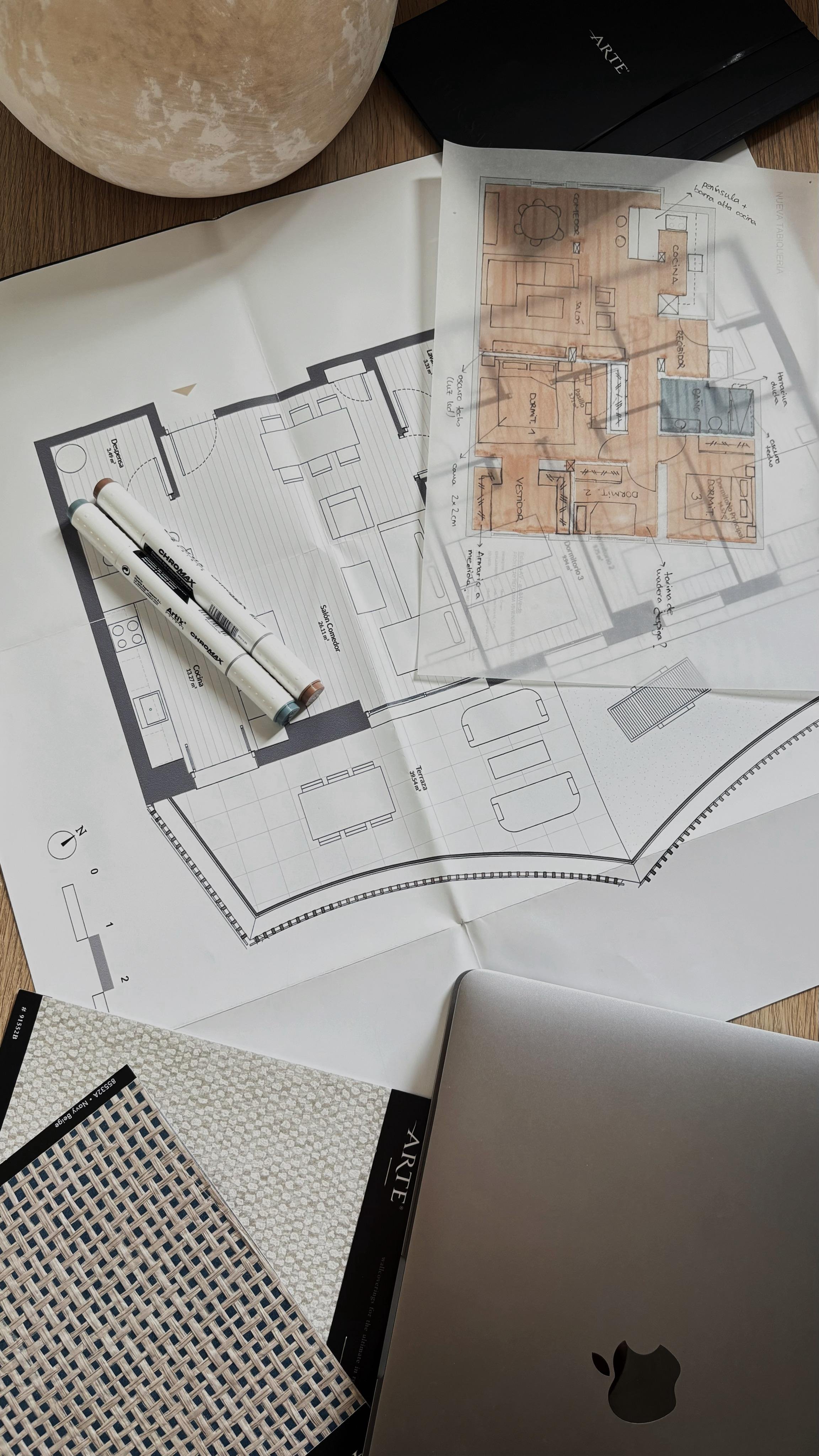 Architectural blueprints and design samples on a desk with a laptop and paint color samples.