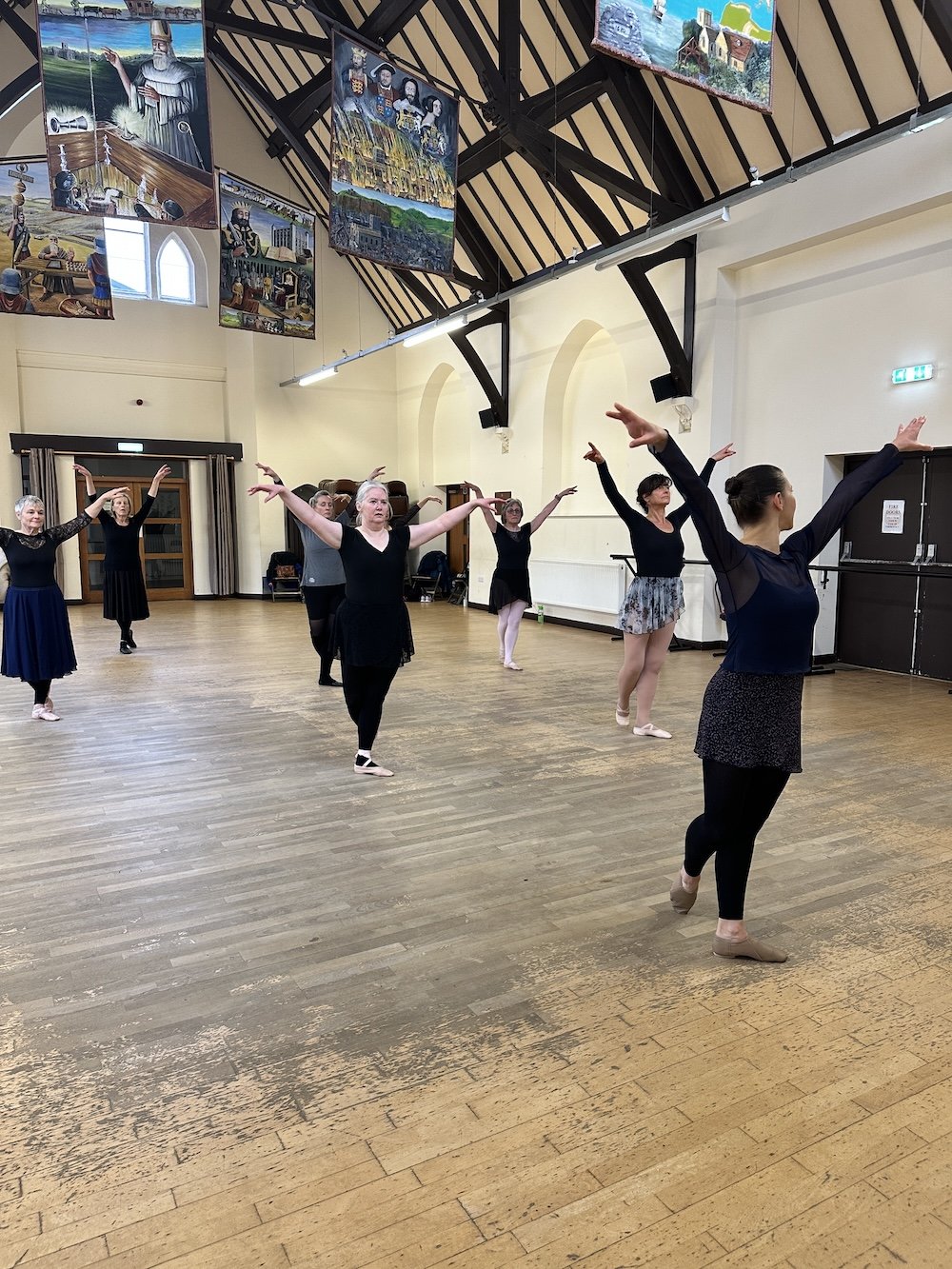 Women practicing ballet in a dance studio with high ceilings and wooden floors