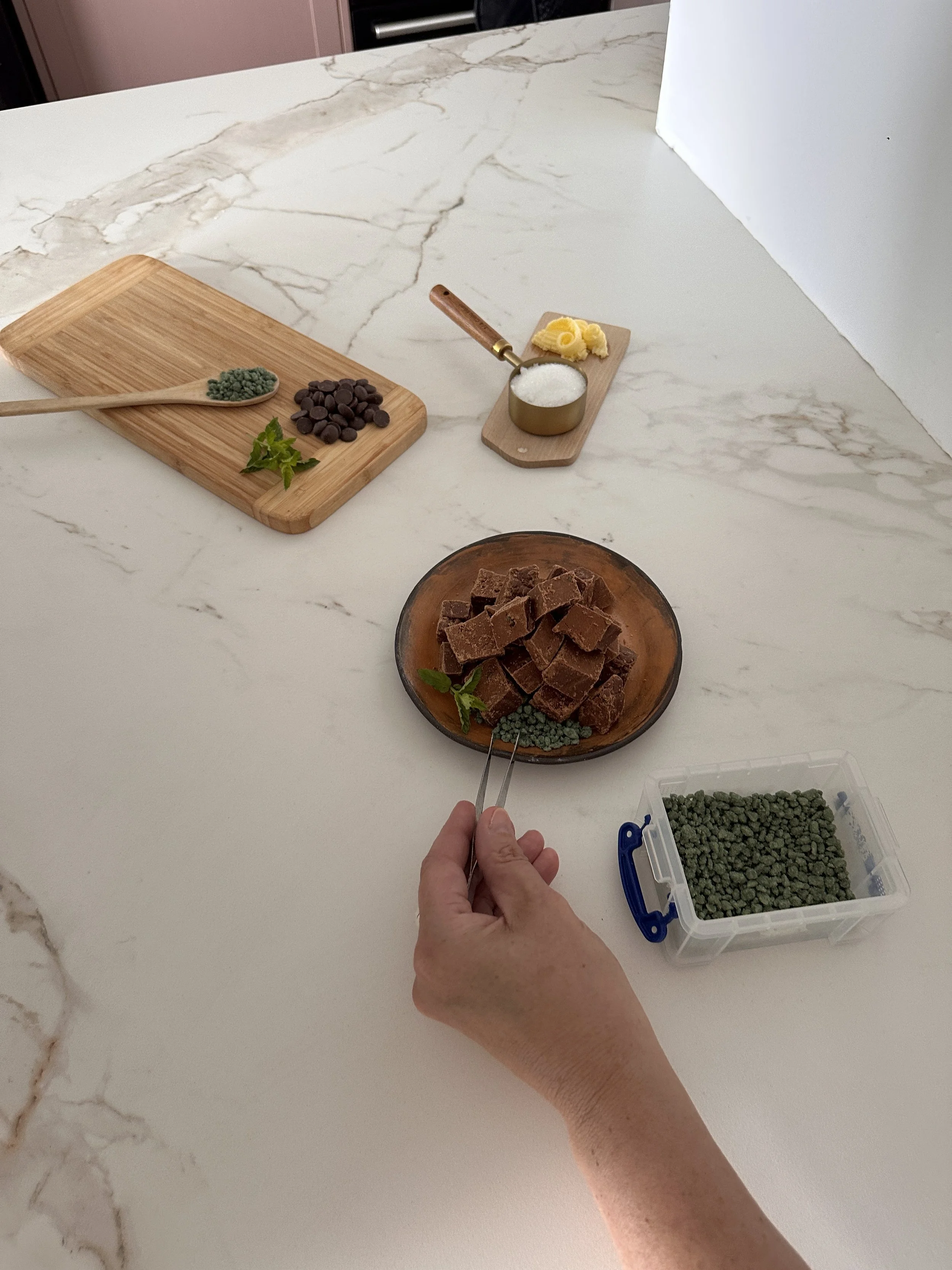Food business owner measuring fudge powder into a glass bowl on a marble countertop