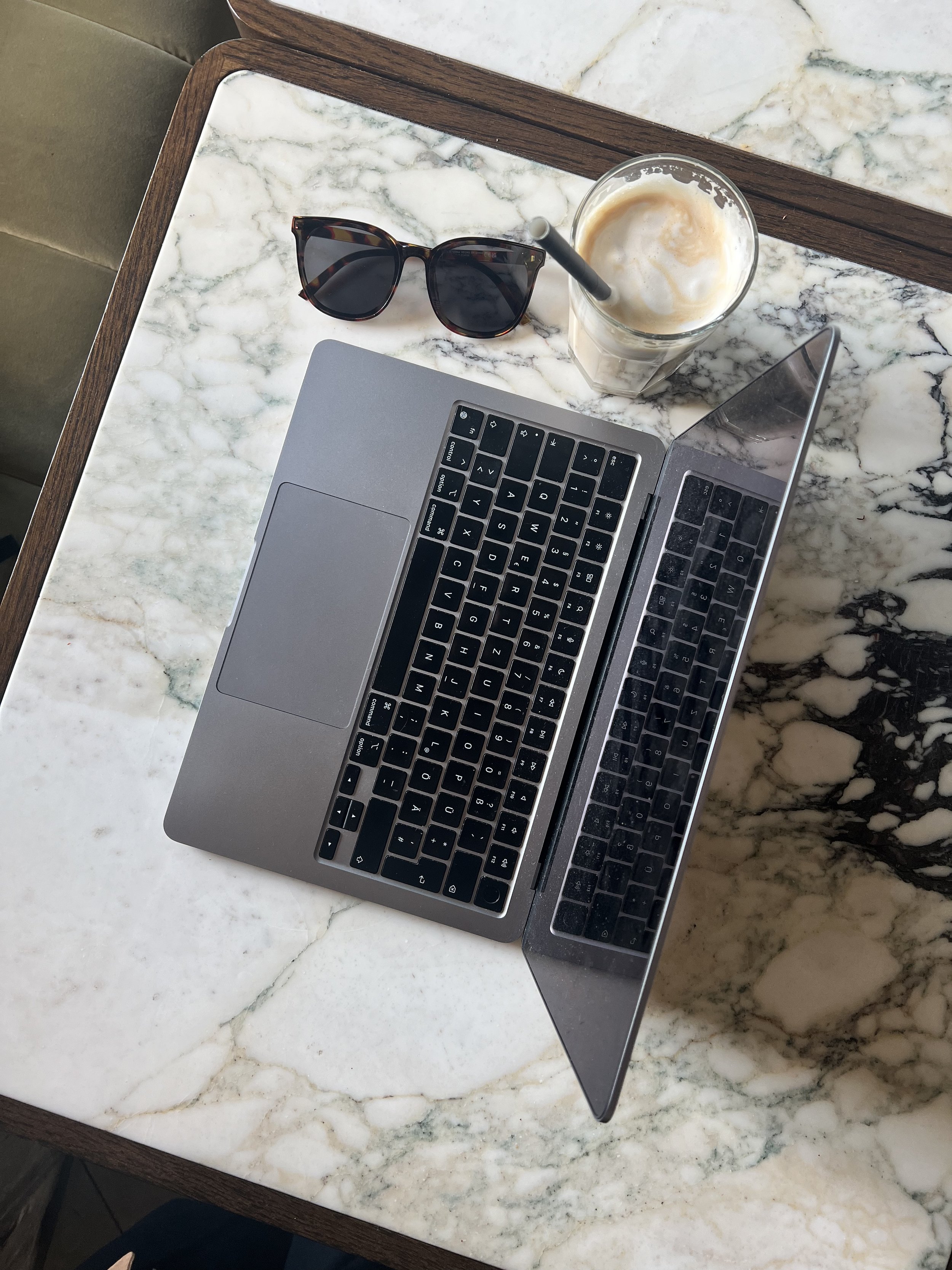 Styled flatlay with a laptop, sunglasses and iced coffee on a marble surface, lifestyle brand aesthetic