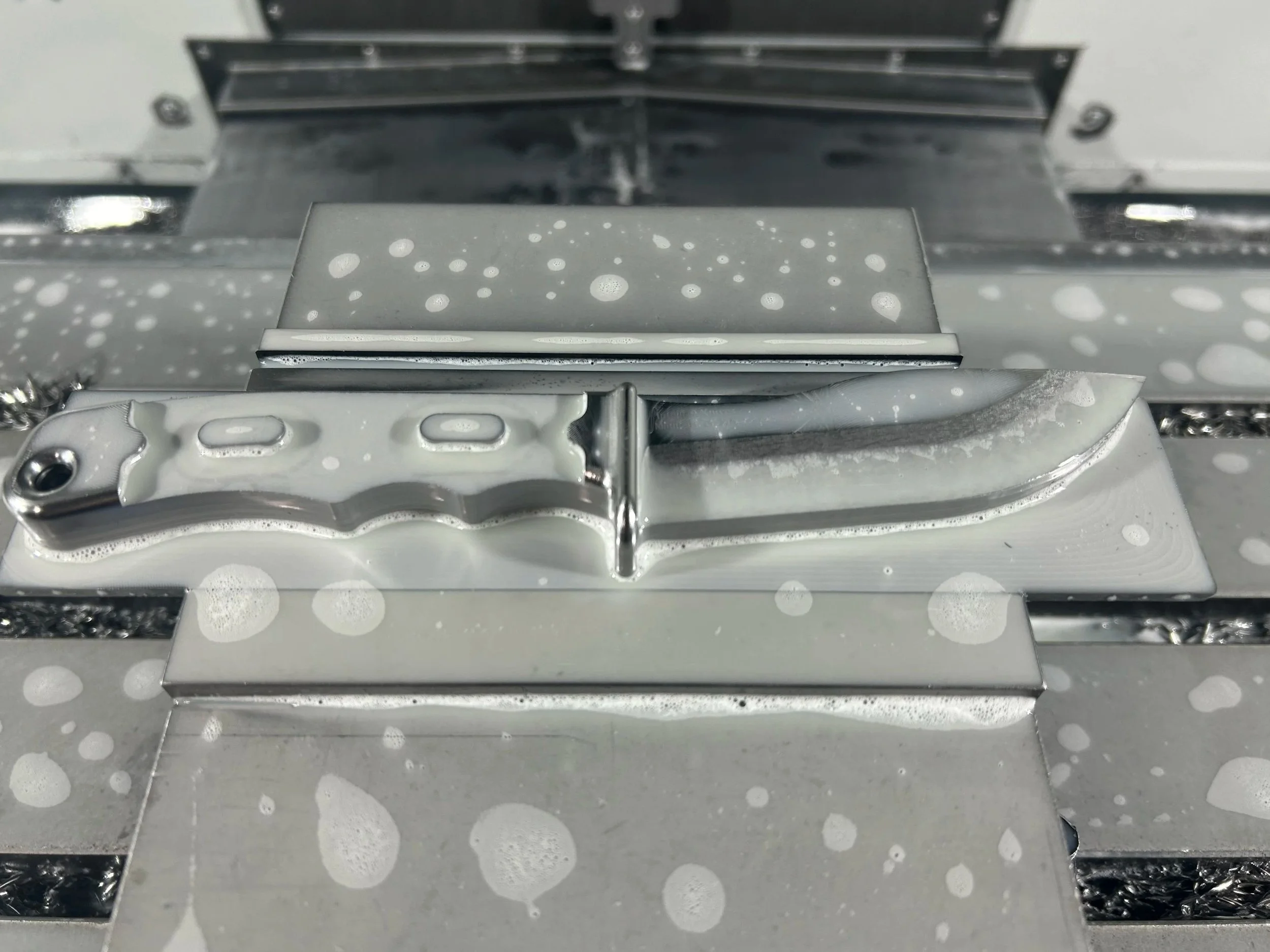 Close-up of a straight razor on a metal surface with soap suds and water droplets.