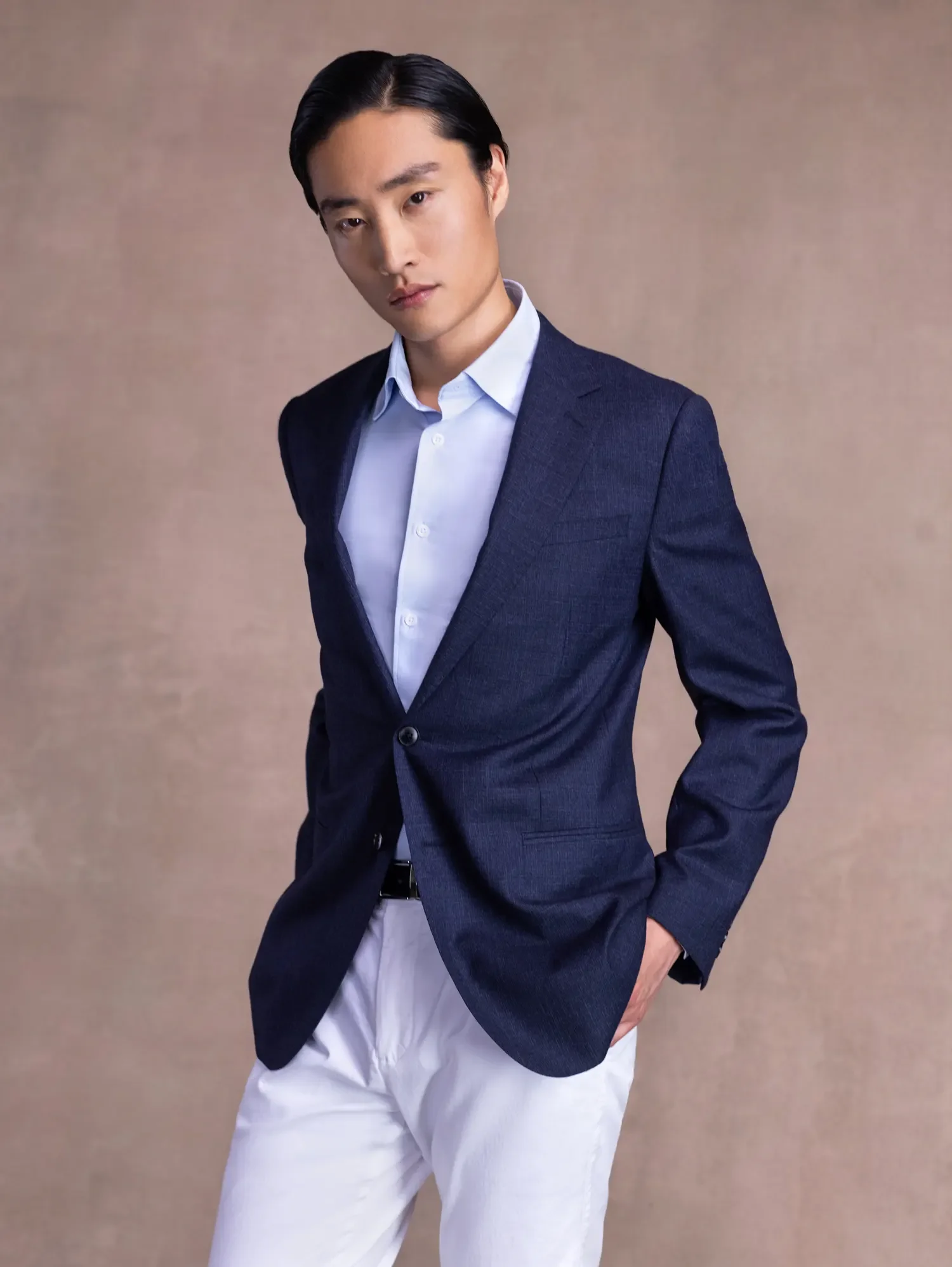 A man with black hair wearing a navy blazer and white shirt, standing against a neutral background.