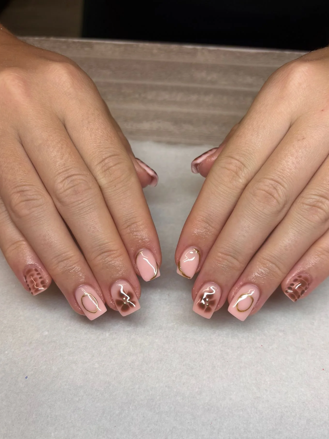 Close-up of fingernails with nude and brown marble design and gold accents.