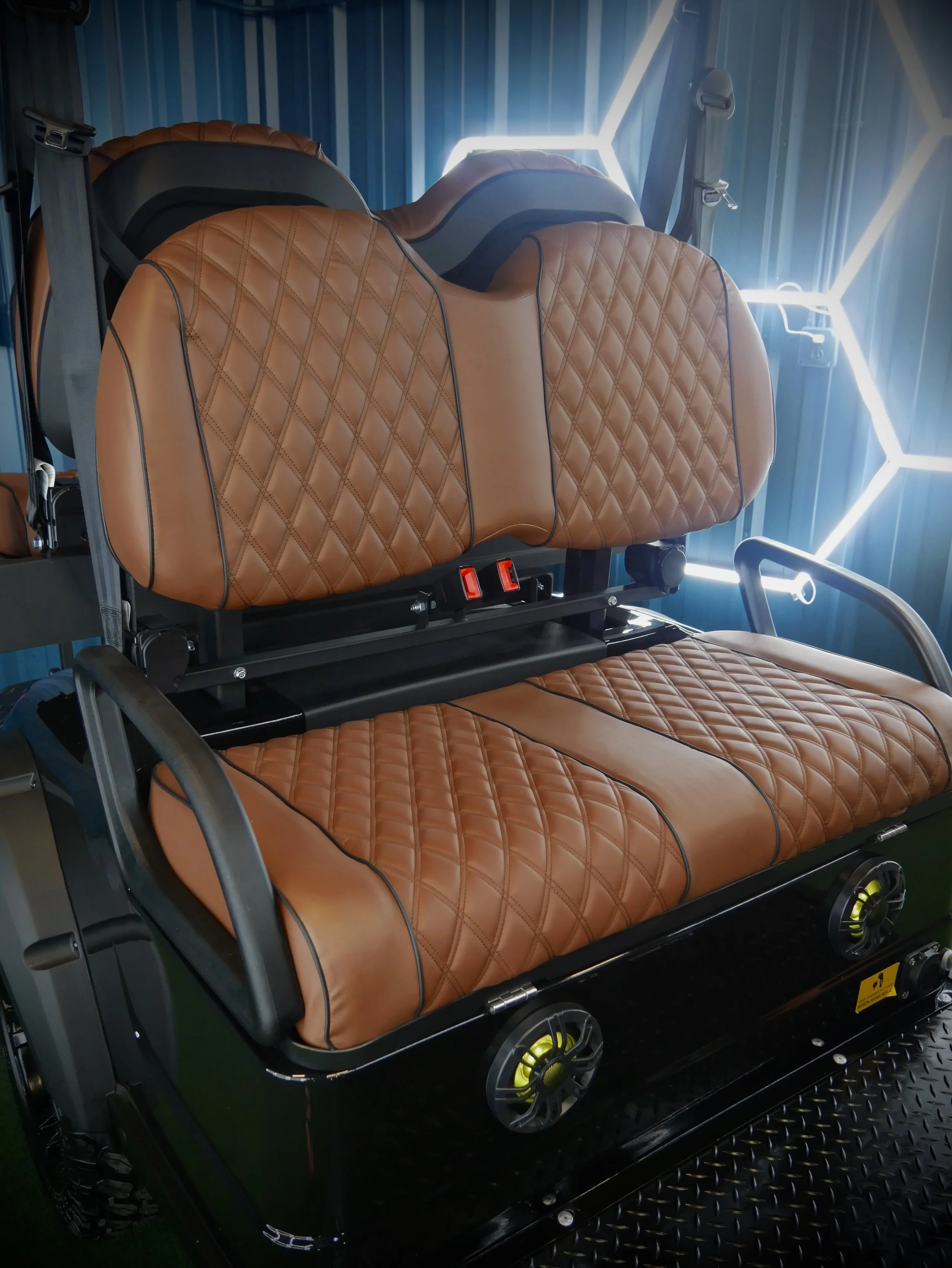 A golf cart with tan quilted leather upholstery and black accents, positioned indoors against a wall with geometric LED lighting