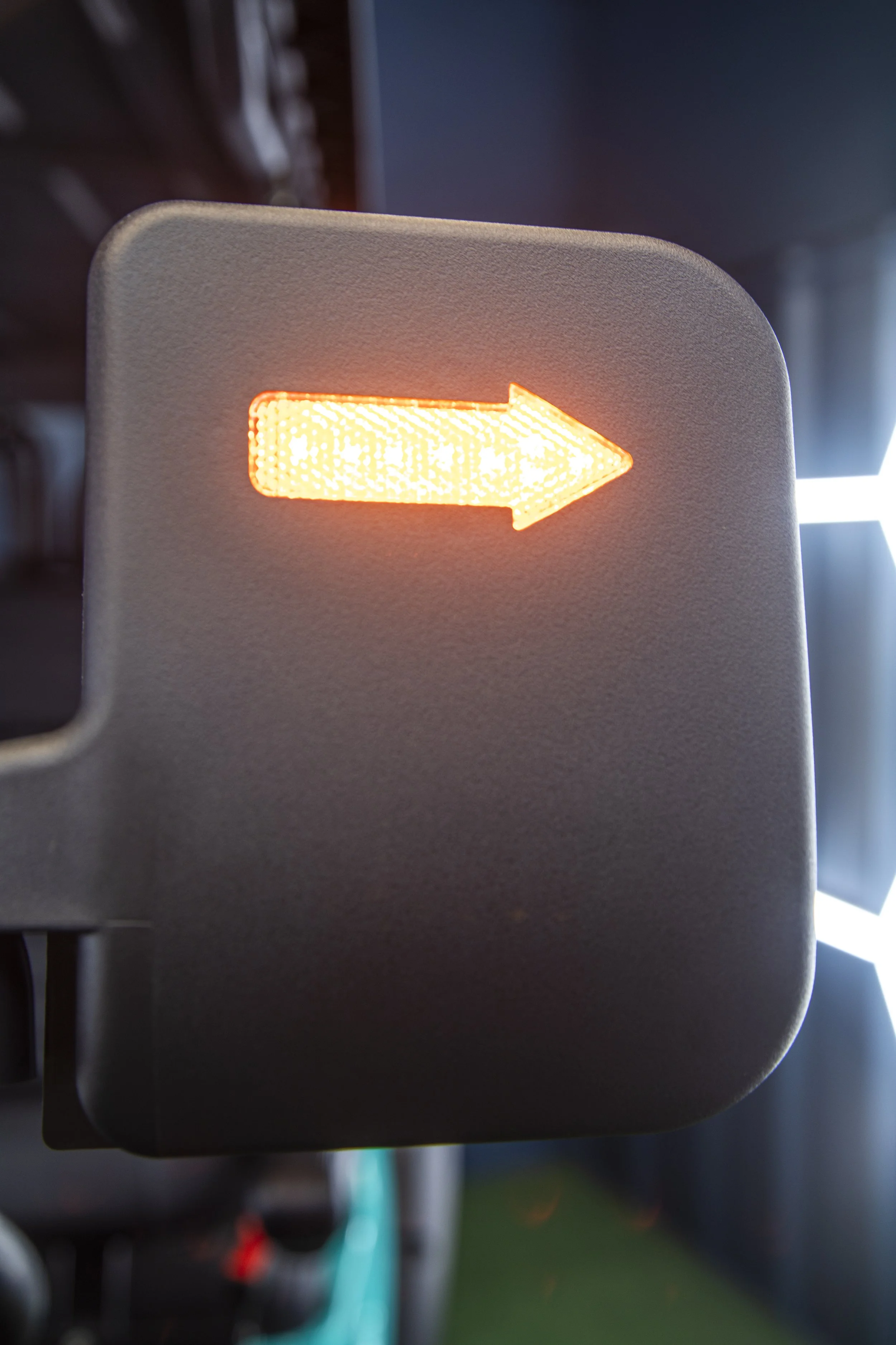 Close-up of a yellow illuminated arrow sign on a wall, pointing to the right, with a blurred background of a classroom or facility.
