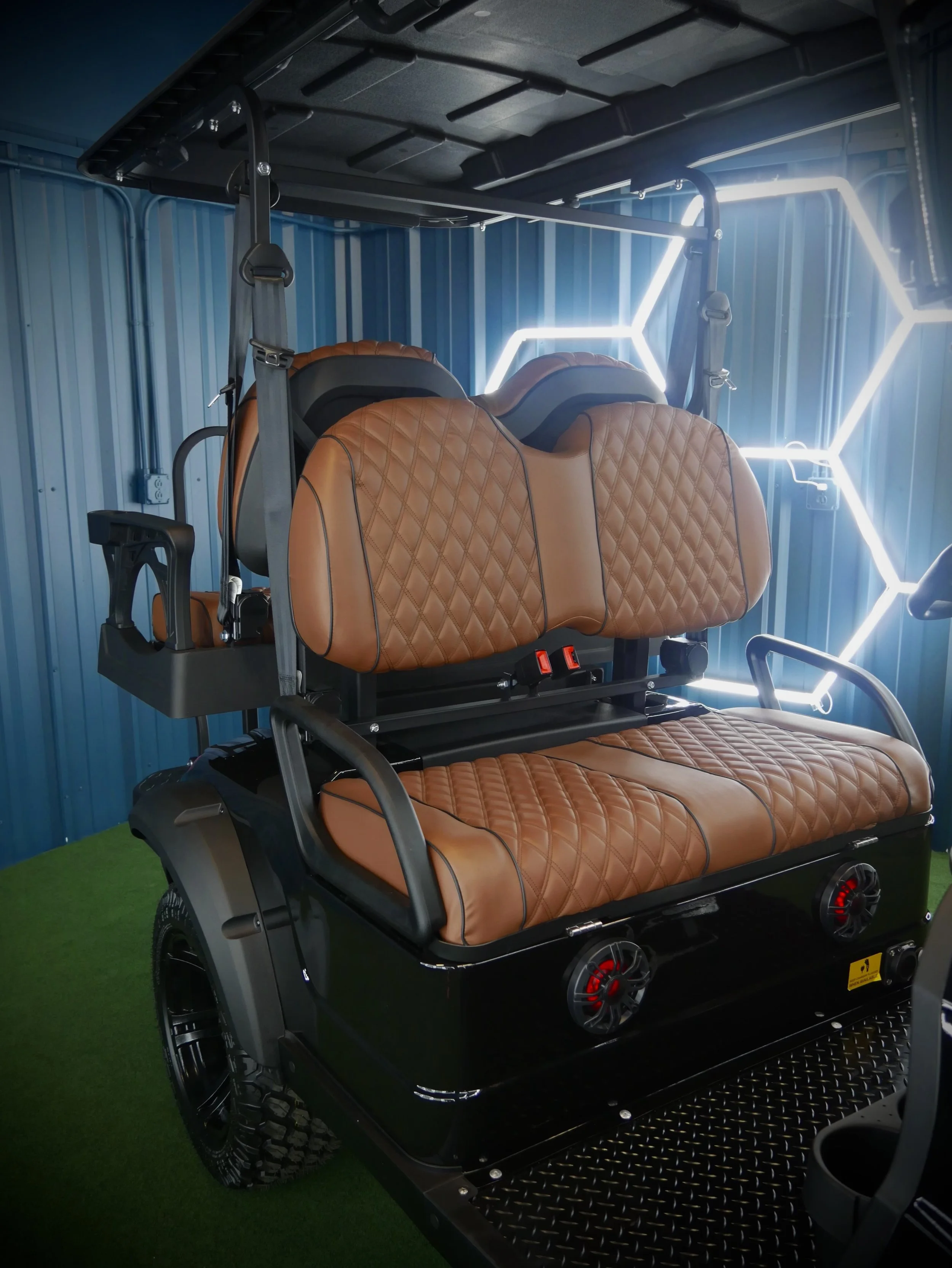 A modern black golf cart with leather seats, large off-road tires, and a black roof inside a modern, industry-inspired space with blue metallic walls and hexagonal lighting.
