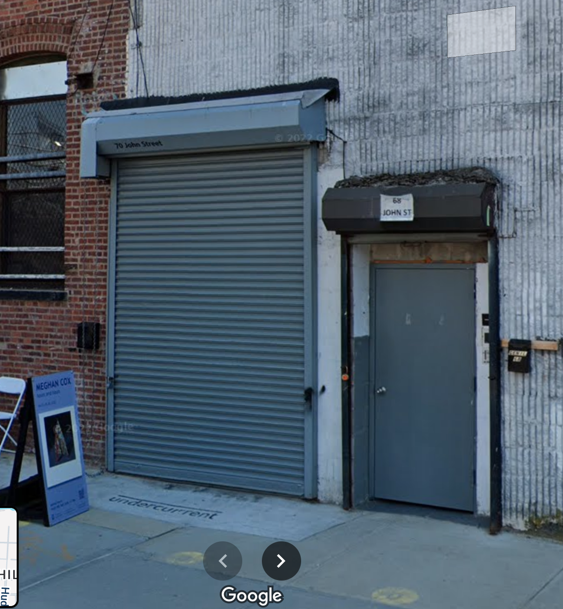 Urban scene with a gray metal security roll-up door, a smaller gray door, and a brick building on the left.