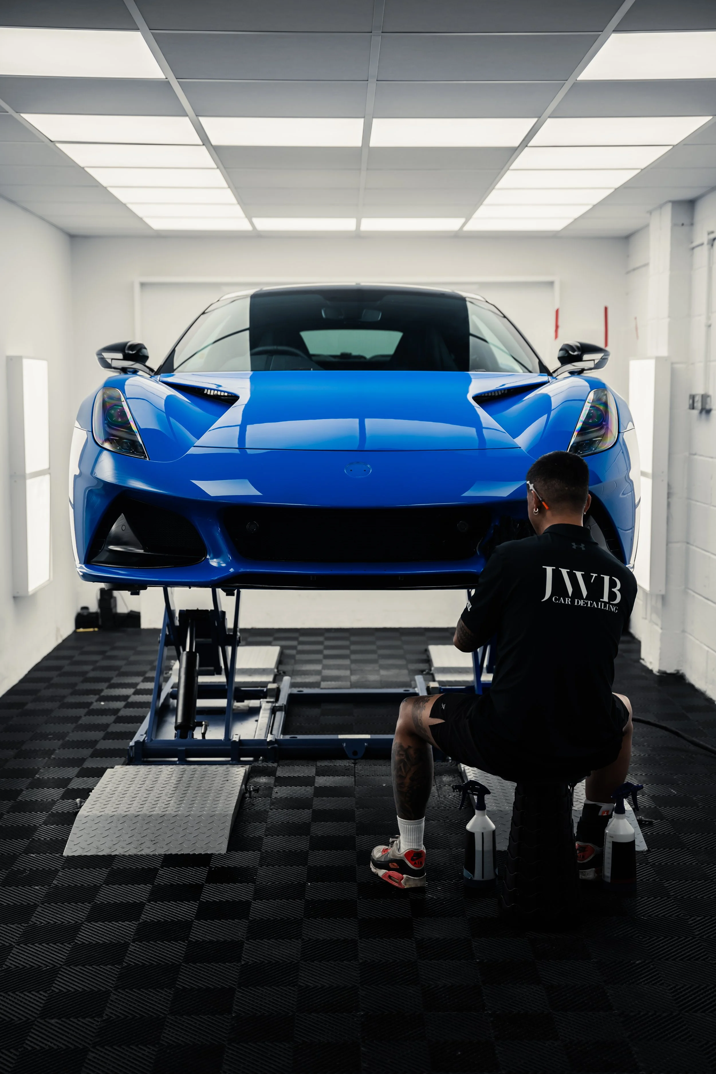 A man working on a blue sports car elevated on a hydraulic lift in a well-lit garage.