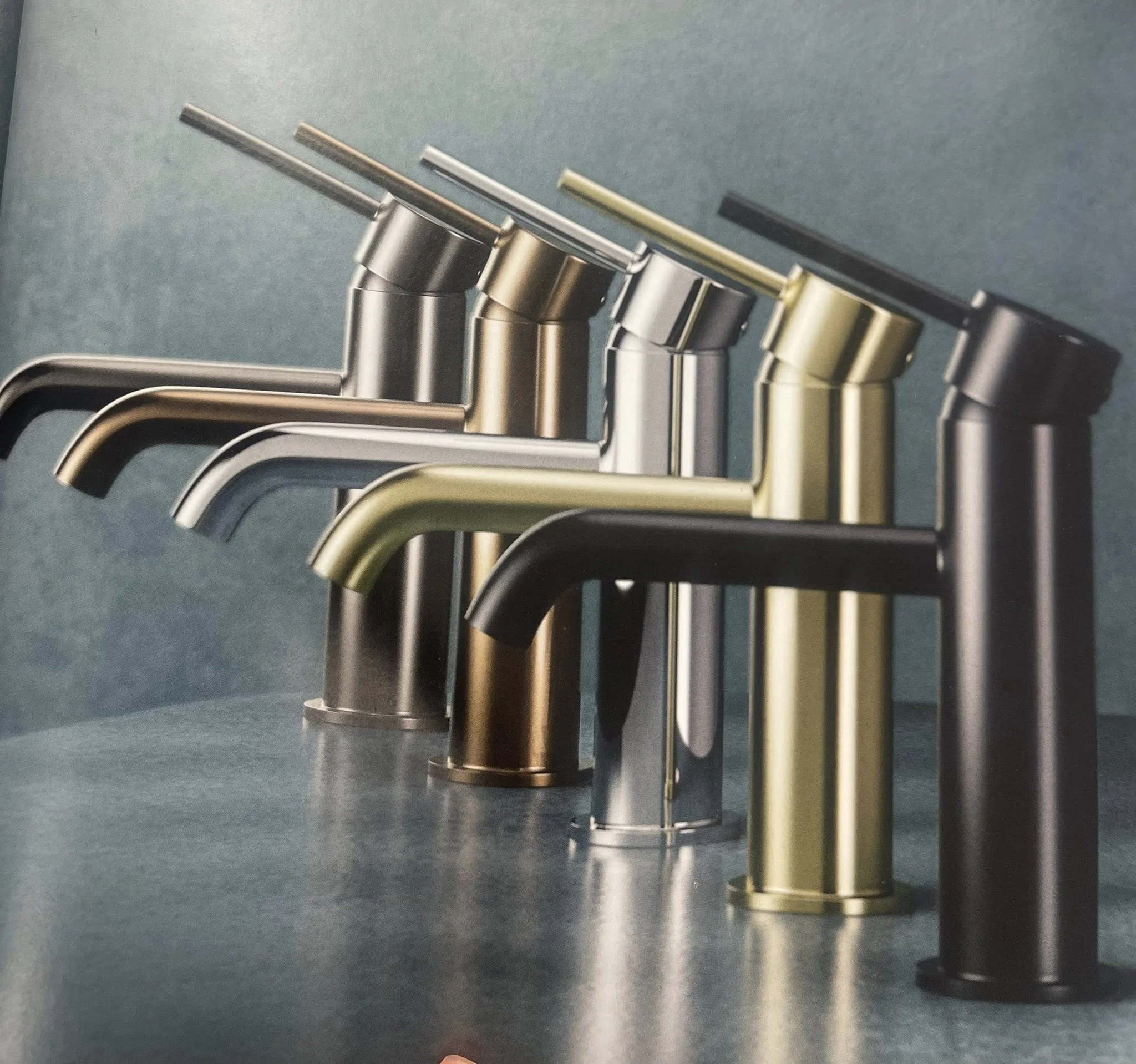 Multiple modern kitchen faucets in various metallic finishes arranged in a row on a countertop.