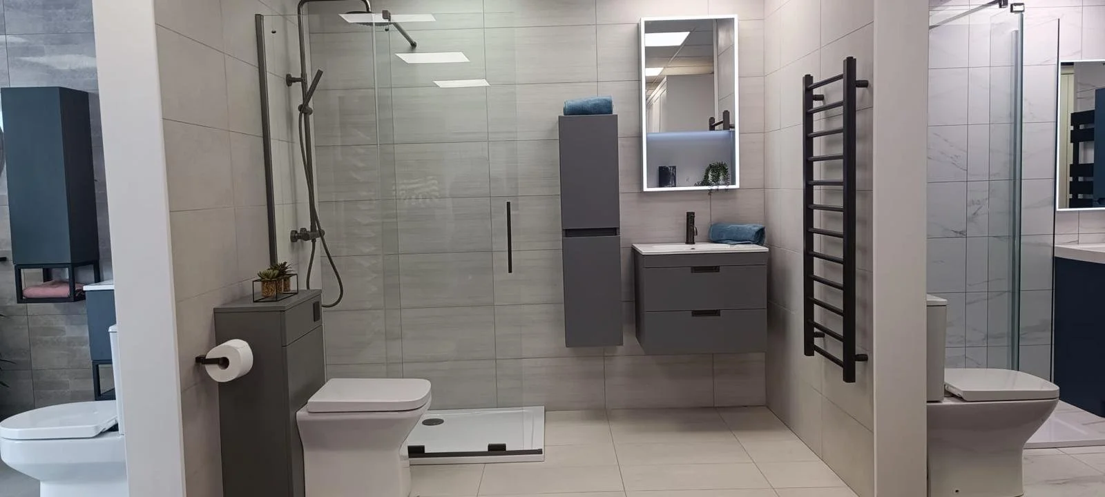 Modern bathroom with a walk-in shower, toilet, and sink with mirror, dark towel rack, and storage cabinets.
