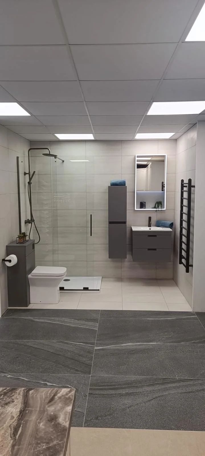 Modern bathroom with tiled walls and ceiling, a walk-in shower with glass enclosure, a toilet, and a vanity with a mirror, towel, and plants.