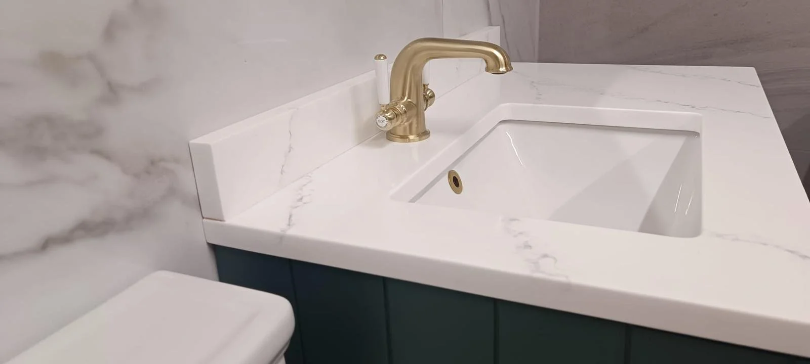 Close-up of a bathroom sink with a gold faucet, white marble countertop, and teal cabinet underneath.